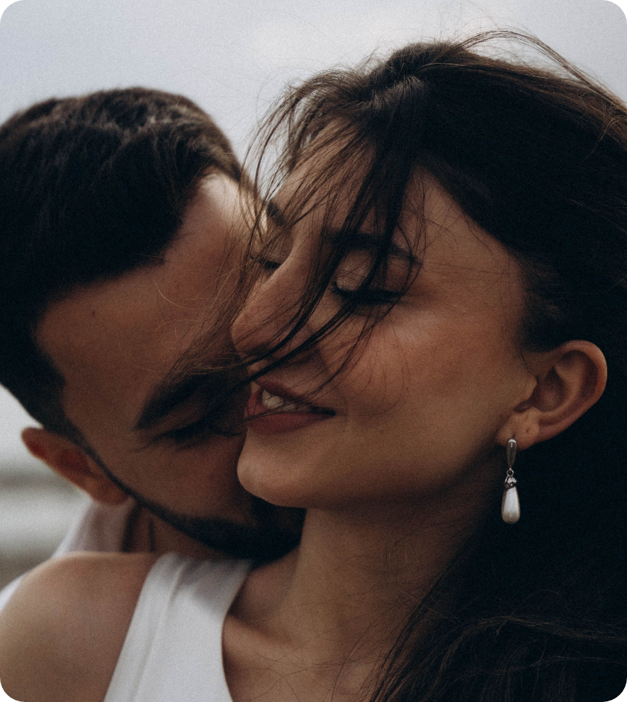 Close-up of a couple sharing an intimate moment, with the man kissing the woman's cheek and the woman smiling with her eyes closed.