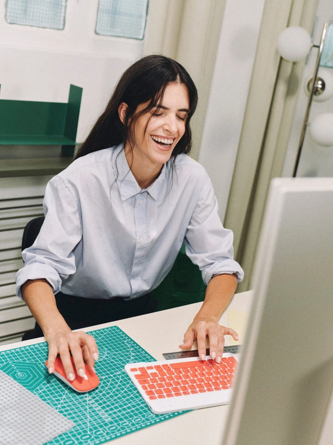 Woman smiling at her work desk with a cutting mat, a computer mouse, and a keyboard.