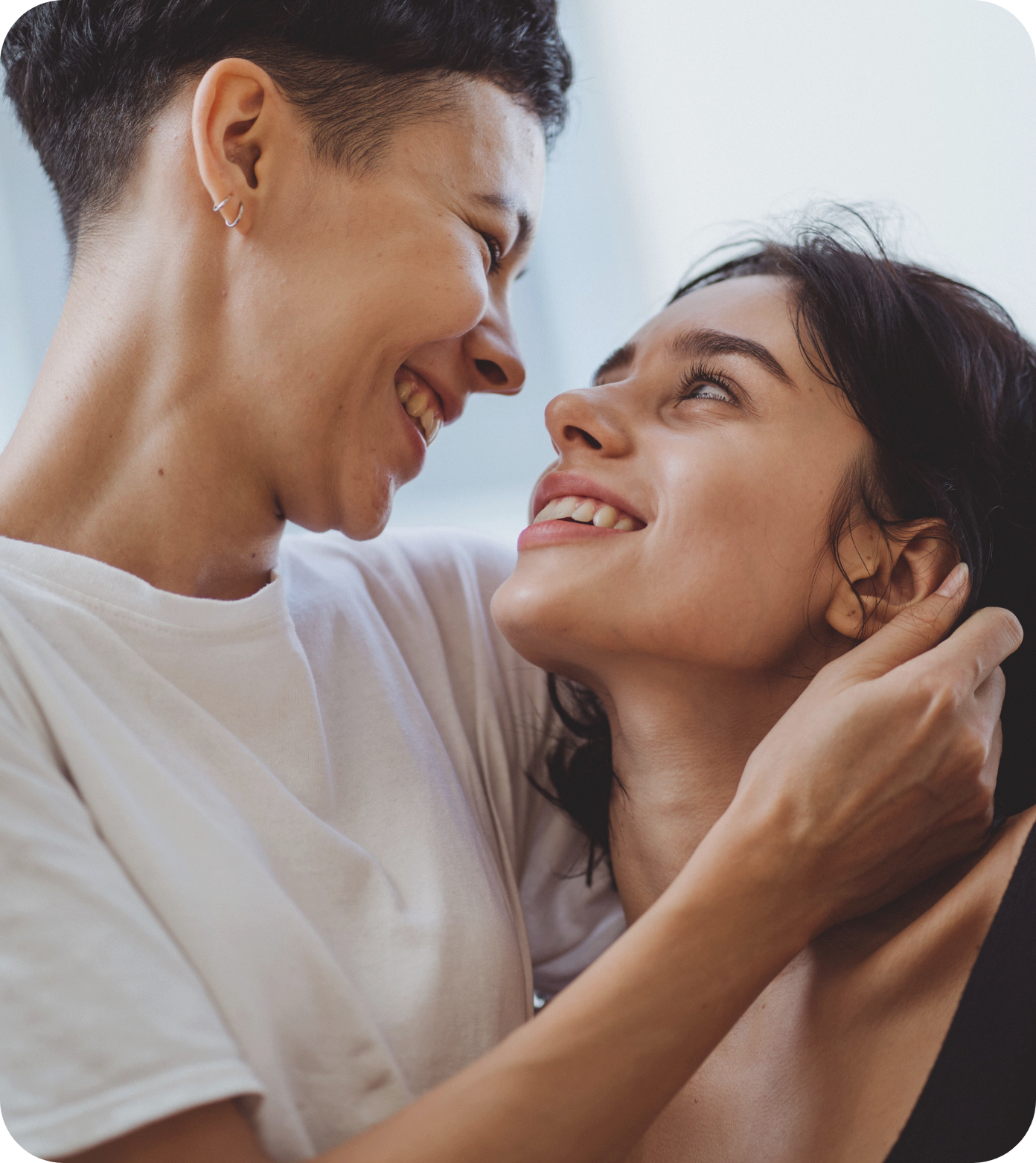 A smiling young couple joyfully looking at each other, sharing an intimate moment indoors.