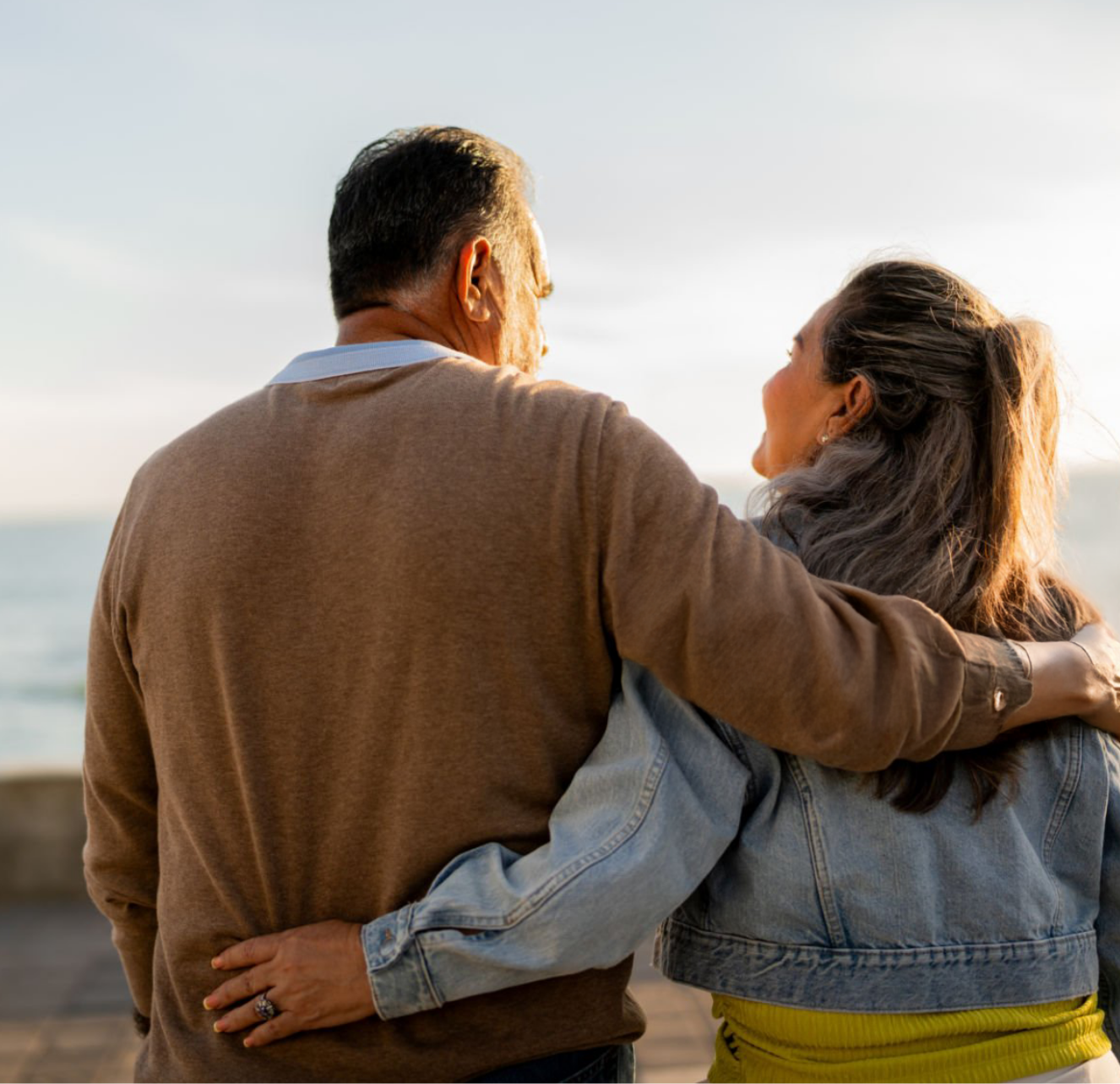 A couple embraces each other at the beach during sunset, with the ocean in the background