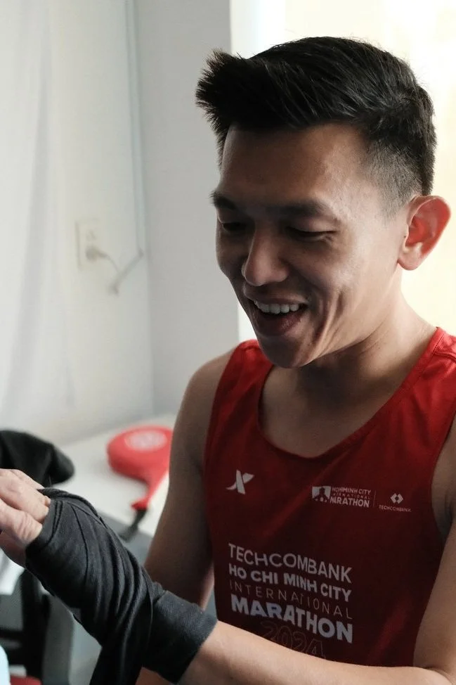 A young man smiling and wearing a red sports jersey with the words 'TECHCOMBANK HO CHI MINH CITY INTERNATIONAL MARATHON' printed on it.
