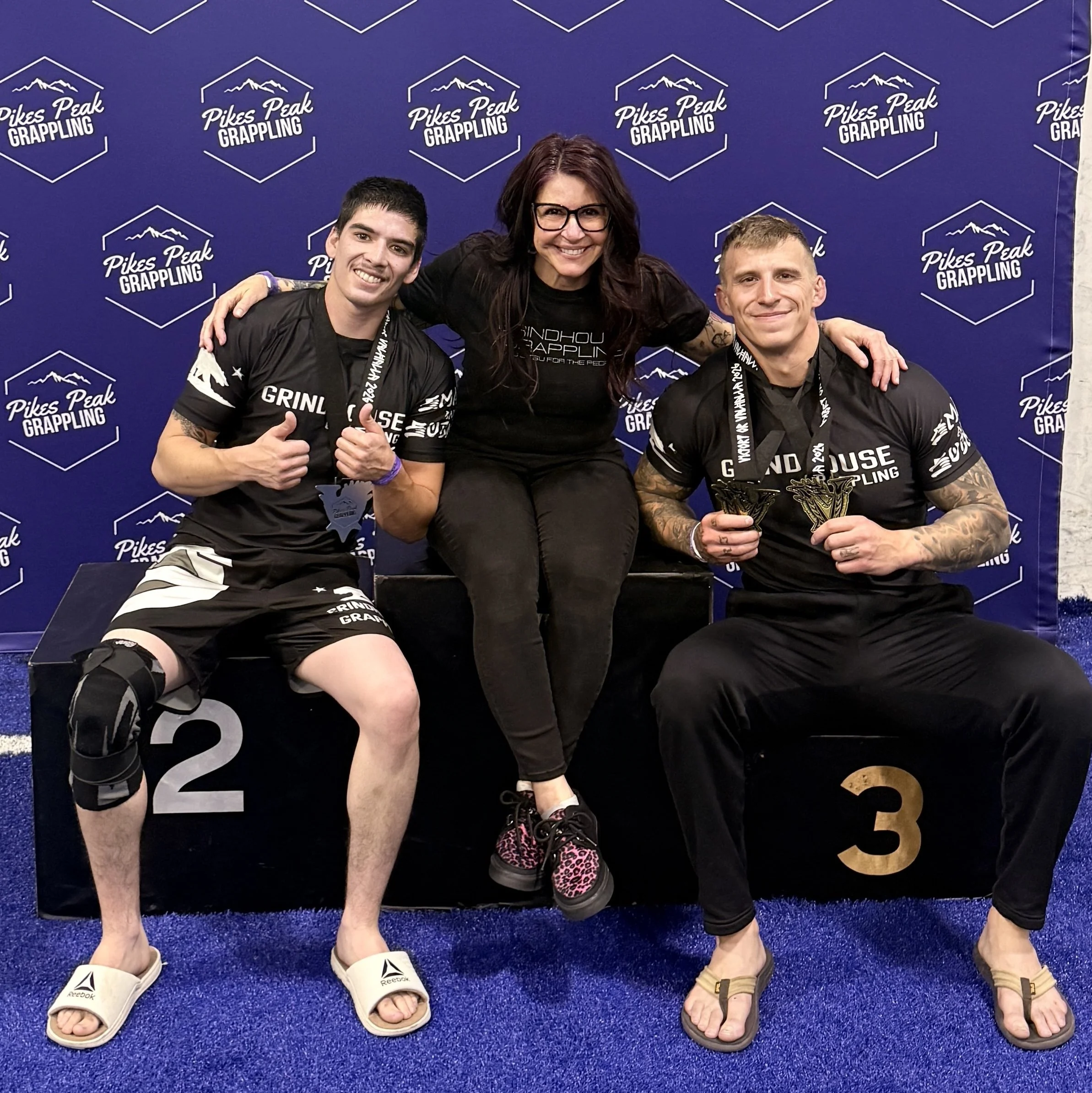 Photo of Coach Denise and two students on the podium at a tournament.