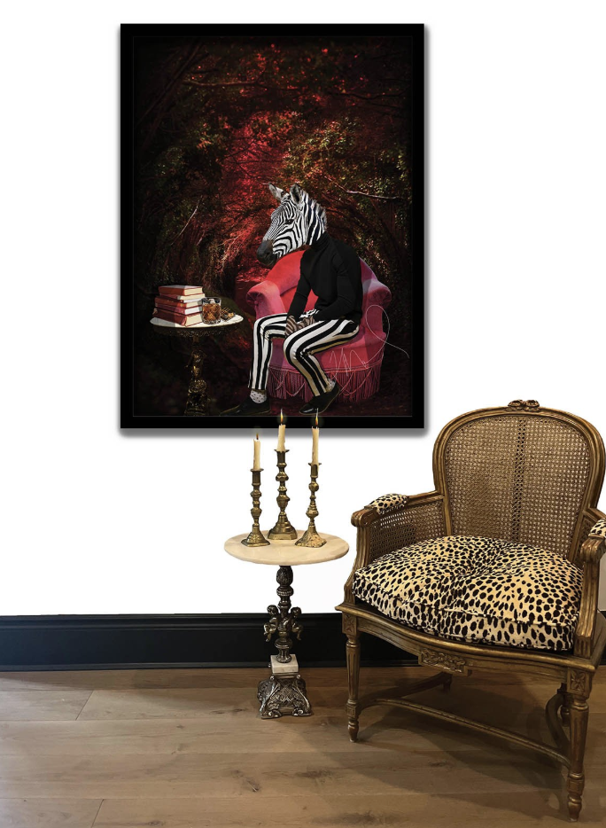 A framed artwork of a person with a zebra head seated in a pink armchair in a forest scene, next to a small table with books and a jar, hangs on a white wall. A vintage wooden chair with leopard print upholstery is placed next to the table, and a candlestick with three candles stands on a small pedestal in front of the chair.