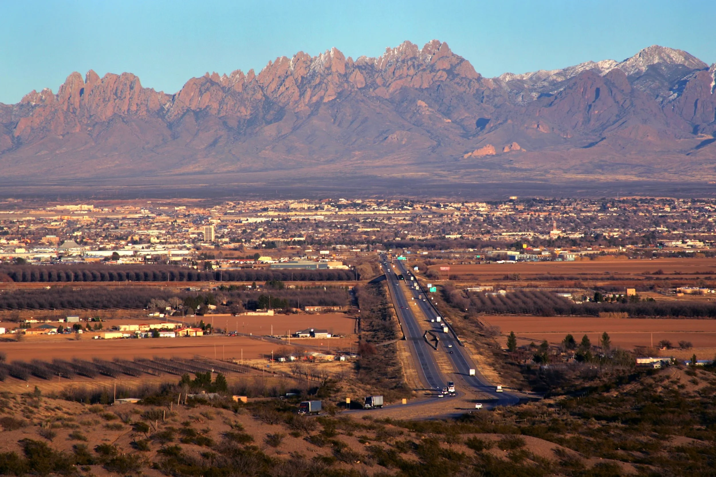 A paved highway stretching through a desert landscape with distant mountains in the background.