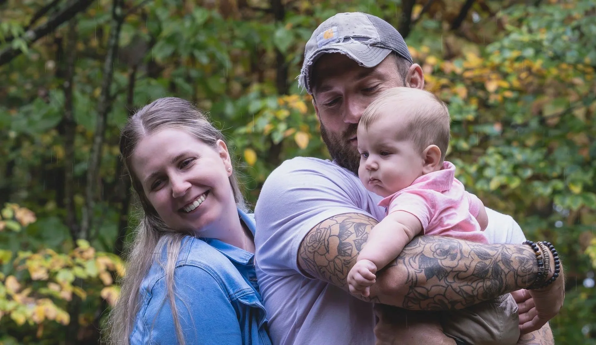 Candid family photo of parents holding their baby outdoors surrounded by greenery