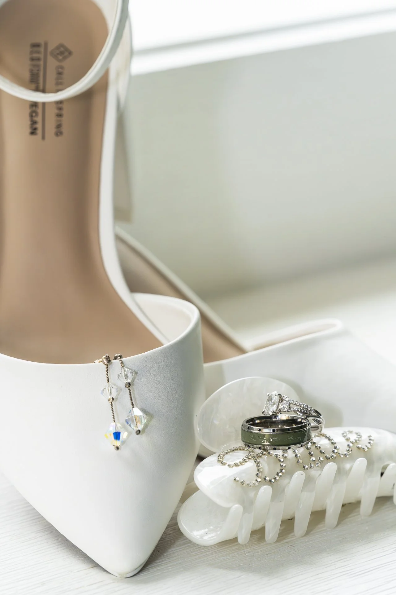 Bridal detail photo of white wedding heels with earrings, engagement ring and wedding band on decorative hair clip, captured by Maryland wedding photographer