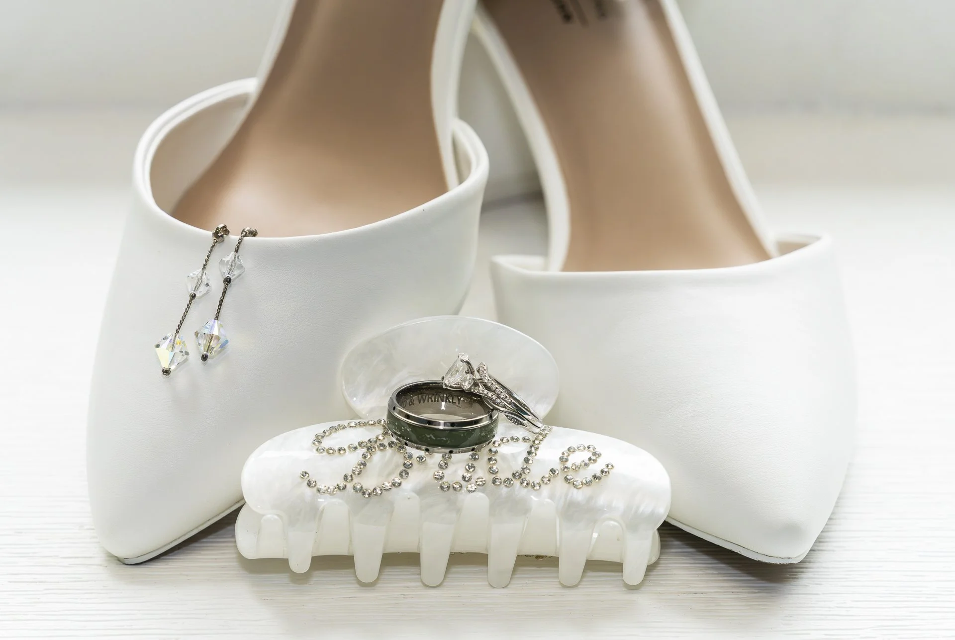 Bridal wedding details featuring white shoes, rings, and jewelry in an elegant minimalist setup