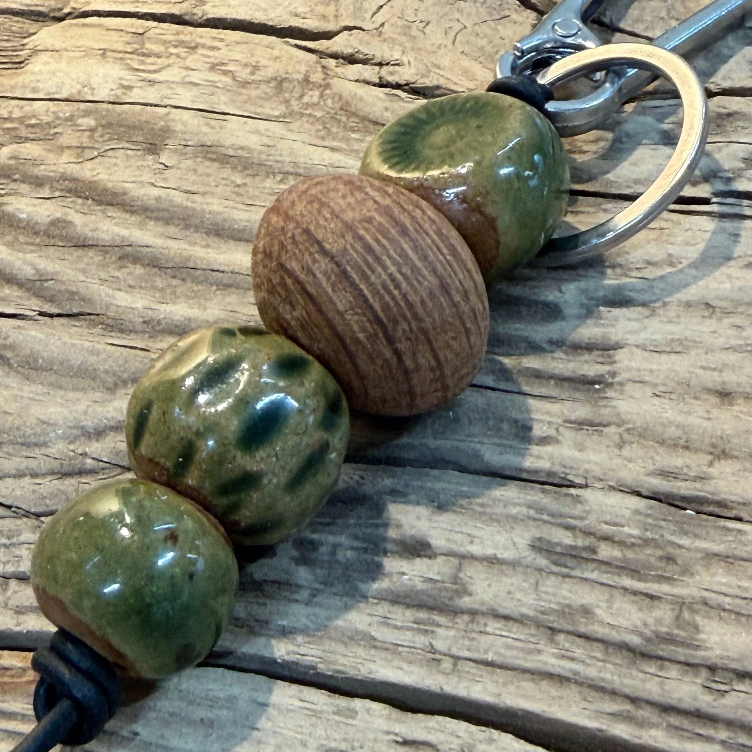 handmade ceramic beads in green and a reclaimed local Kalgoorlie Goldfields timber bead and is attached to a platinum silver plated iron swivel clasp on leather cord.