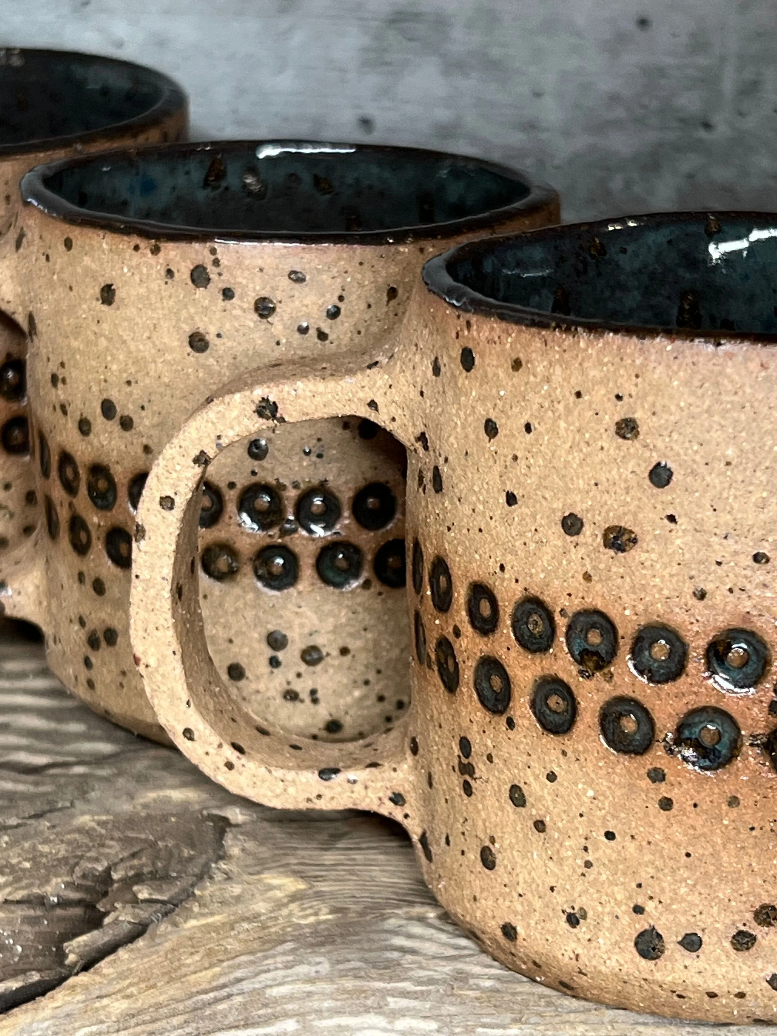 Close-up of three ceramic coffee mugs with black speckled pattern and black interiors, placed on a wooden surface.