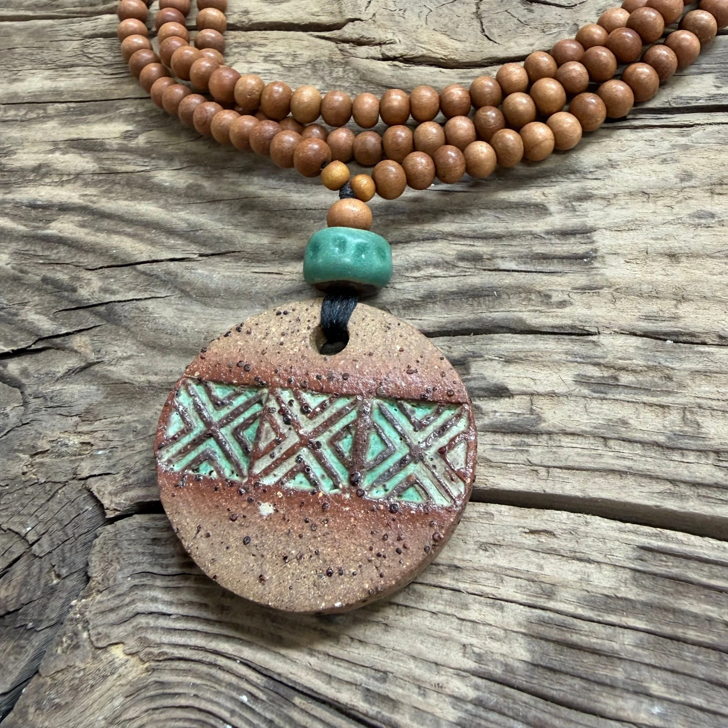 textured stoneware clay pendant with a geometric pattern  and is finished with a green glaze inlay.