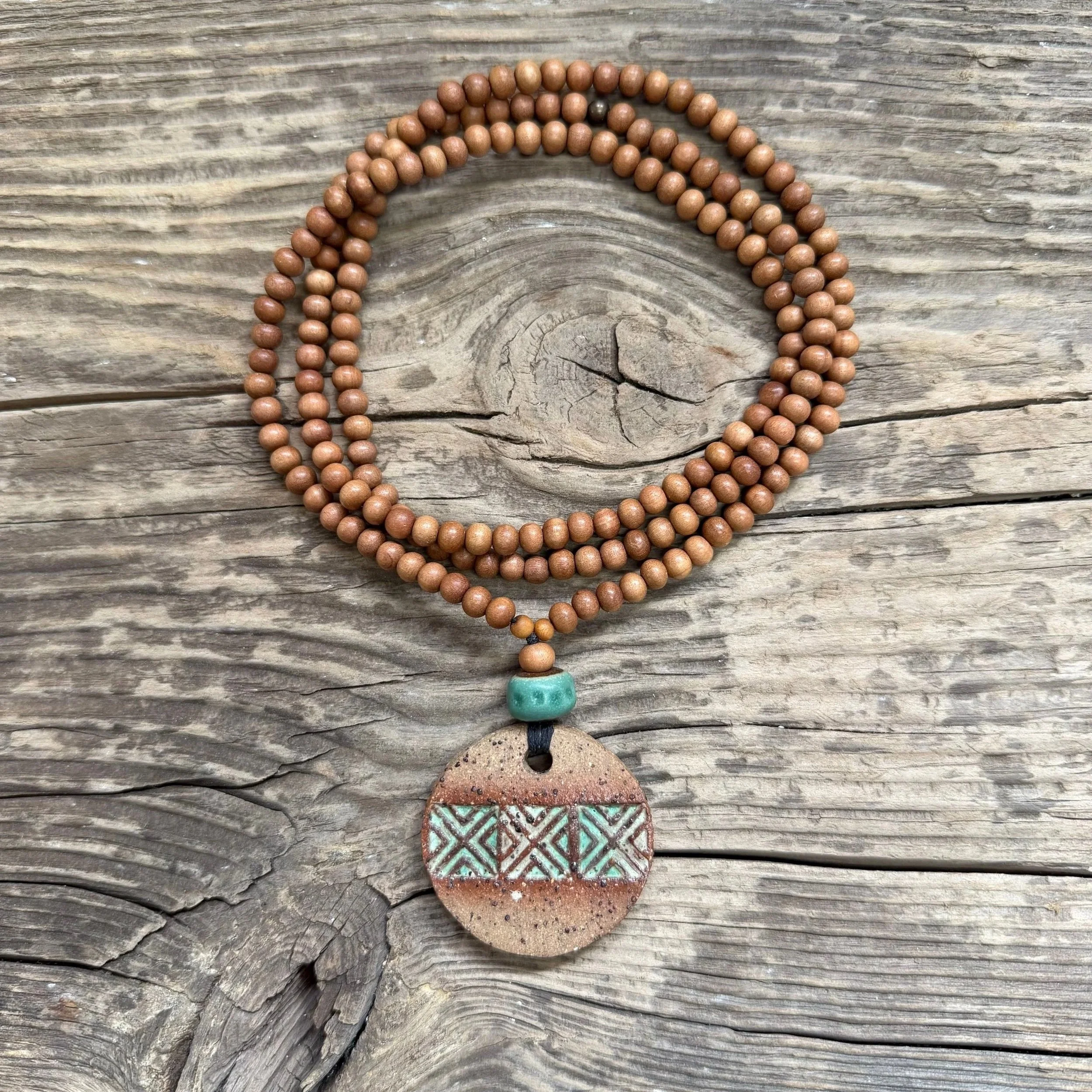 textured stoneware clay pendant with a geometric pattern  and is finished with a green glaze inlay.