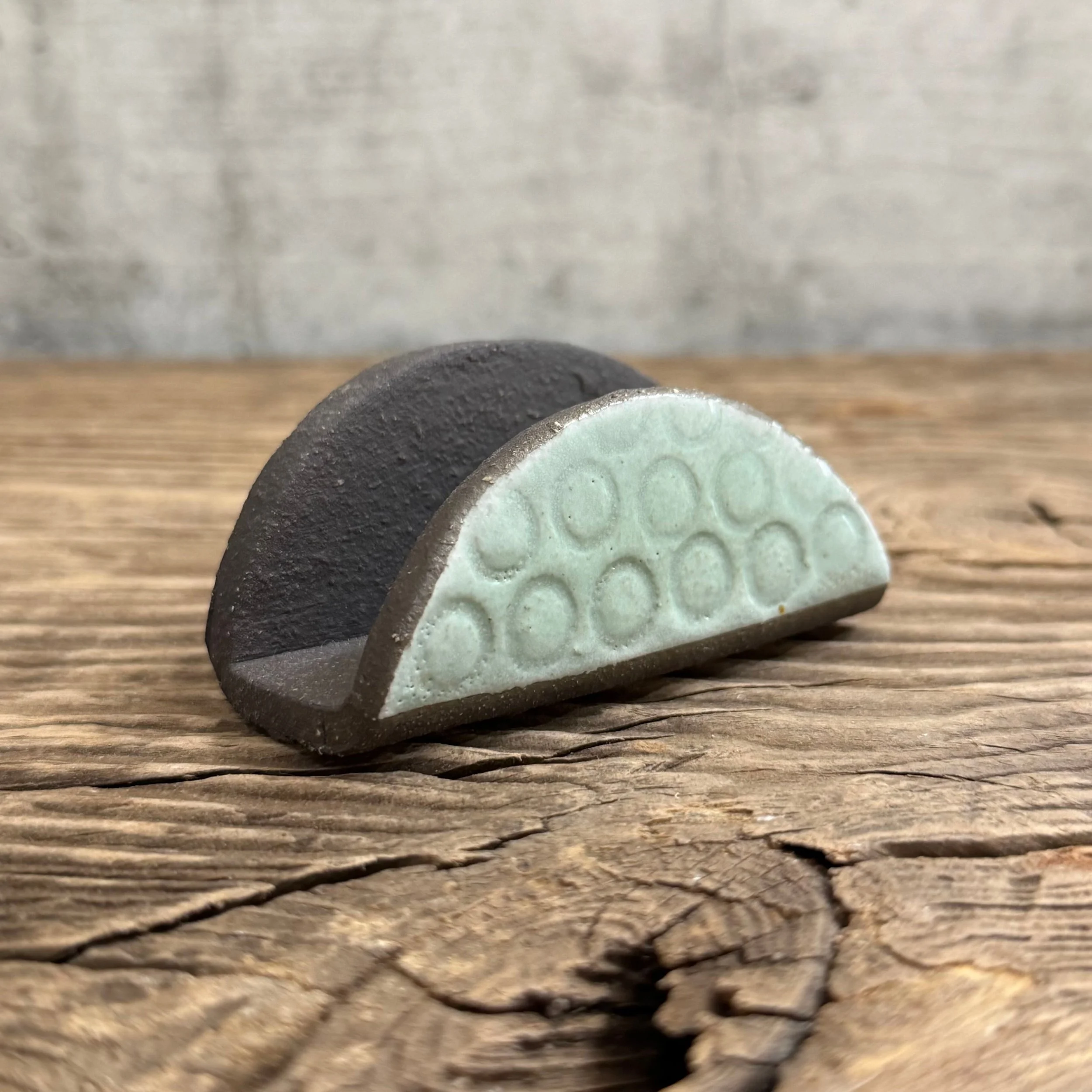 A textured handmade ceramic business card holder made from black clay with a mint finish.