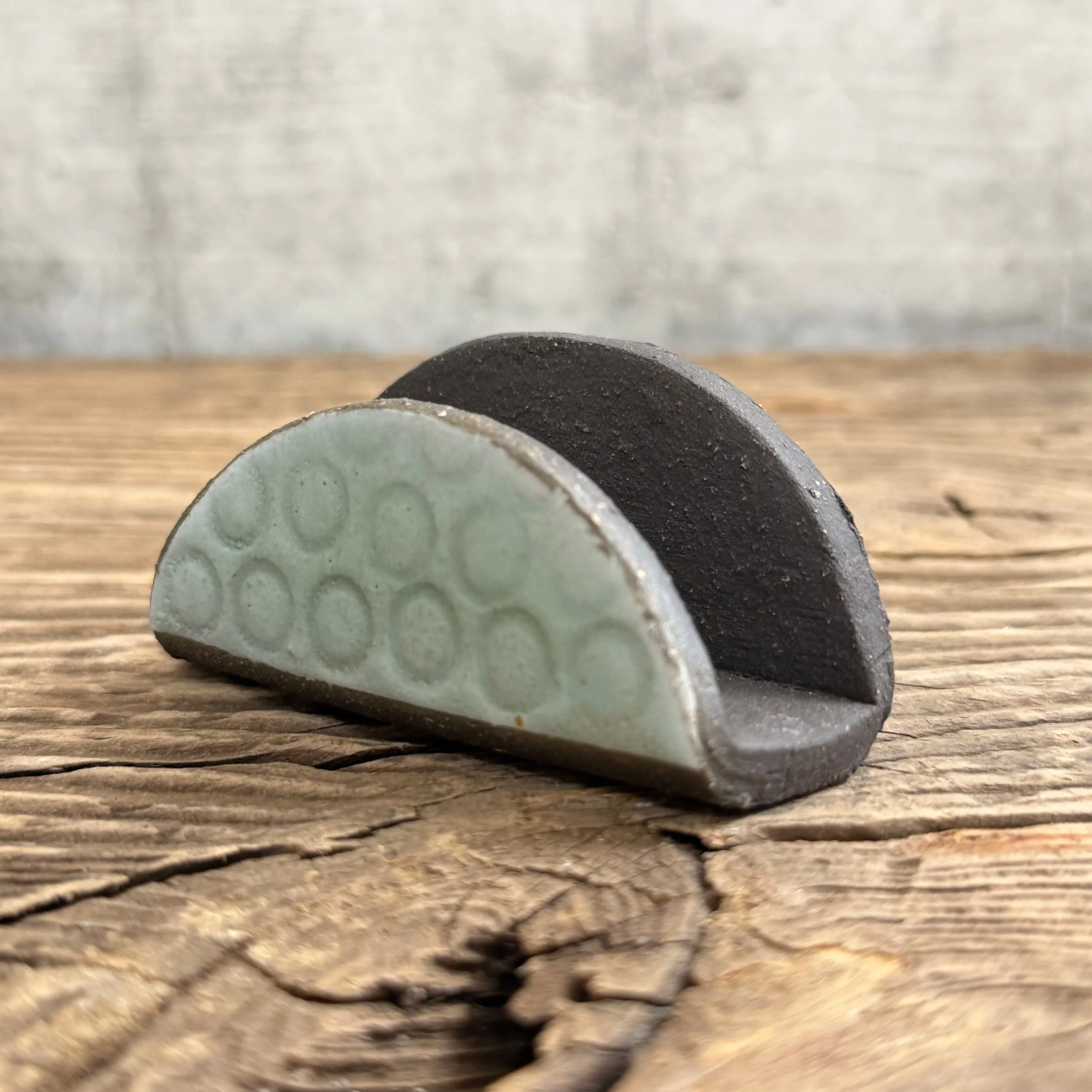 A textured handmade ceramic business card holder made from black clay with a mint finish.