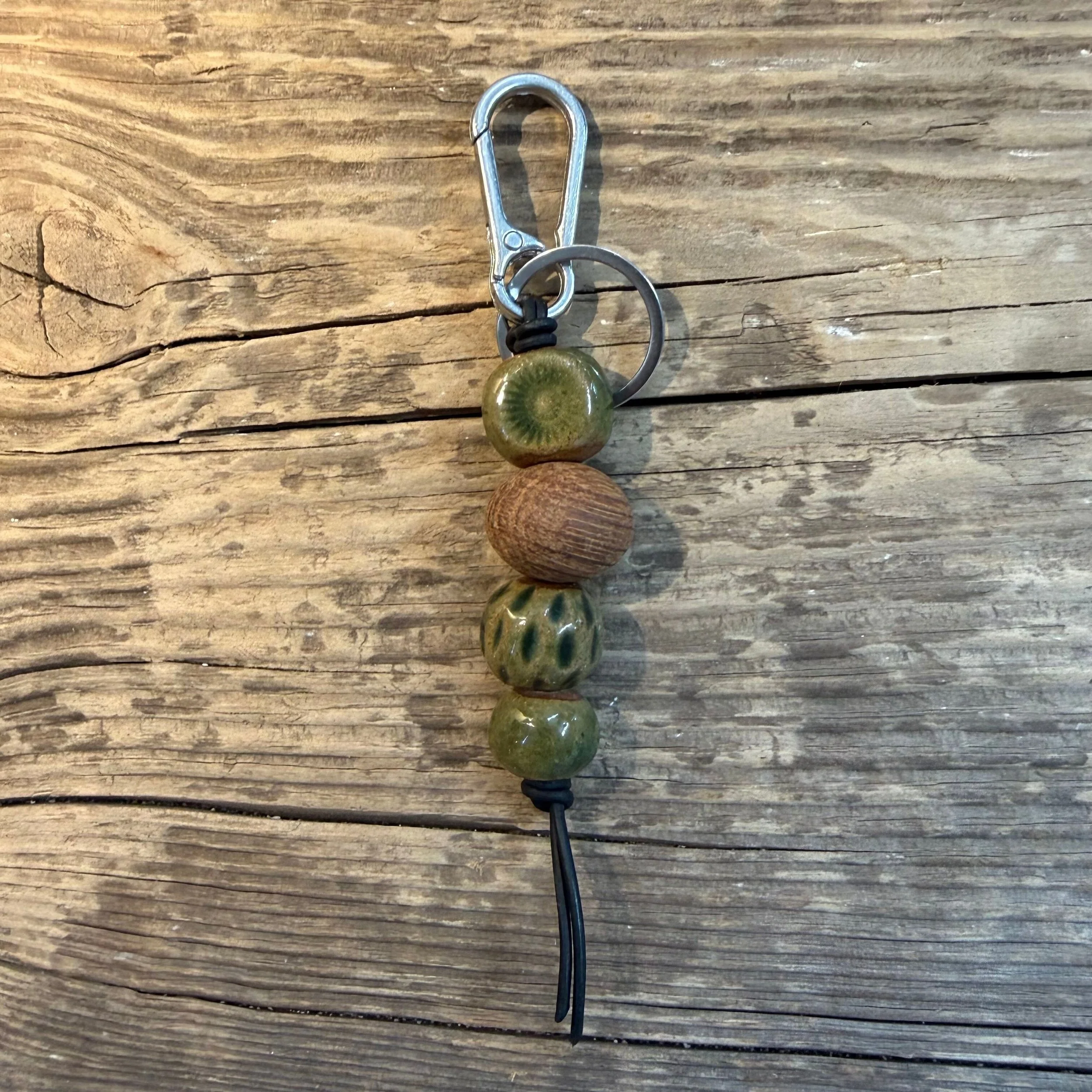 handmade ceramic beads in green and a reclaimed local Kalgoorlie Goldfields timber bead and is attached to a platinum silver plated iron swivel clasp on leather cord.
