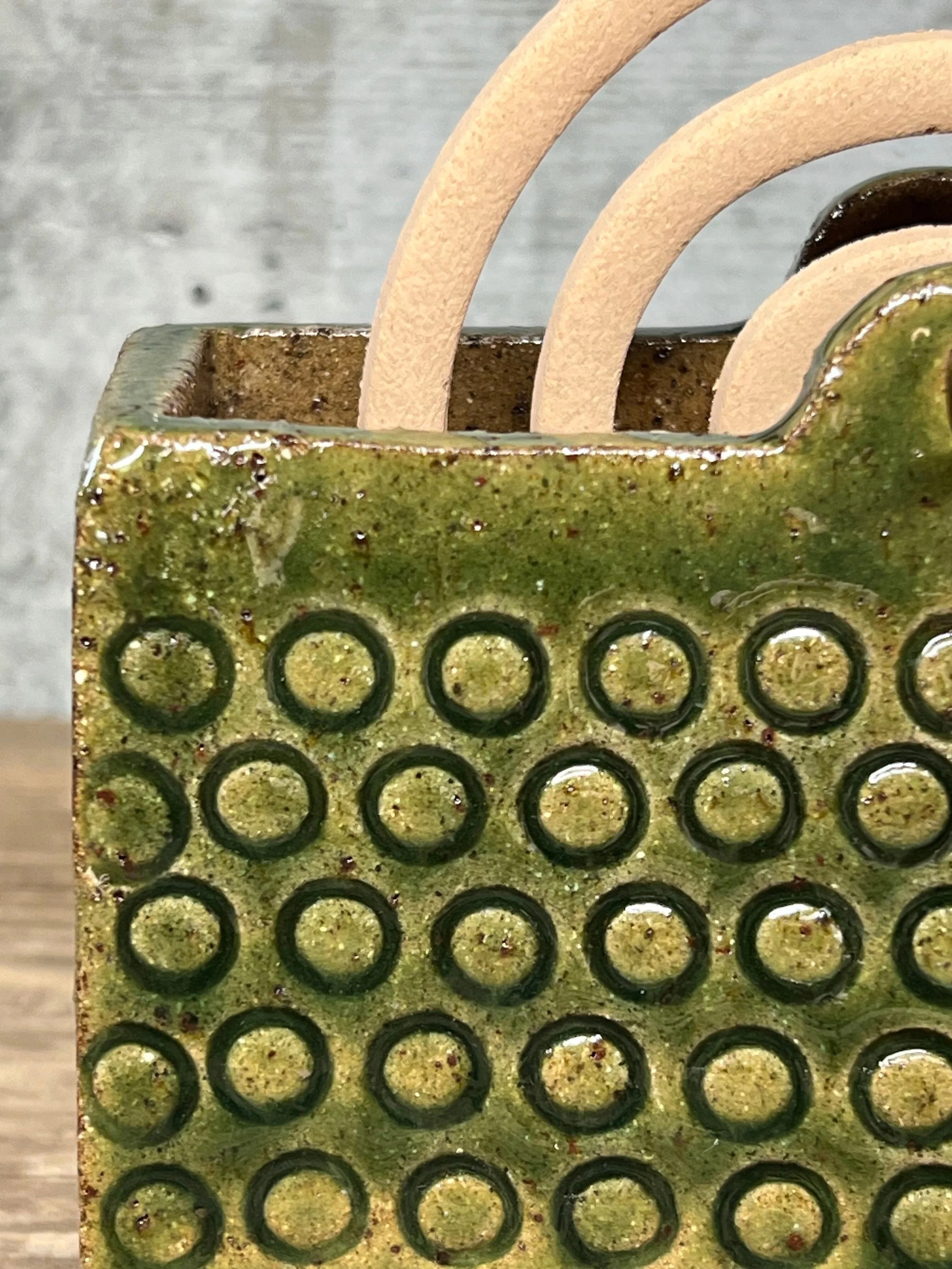 handcrafted mozzie coil holder, made from durable stoneware clay and finished with a transparent dark green glaze.