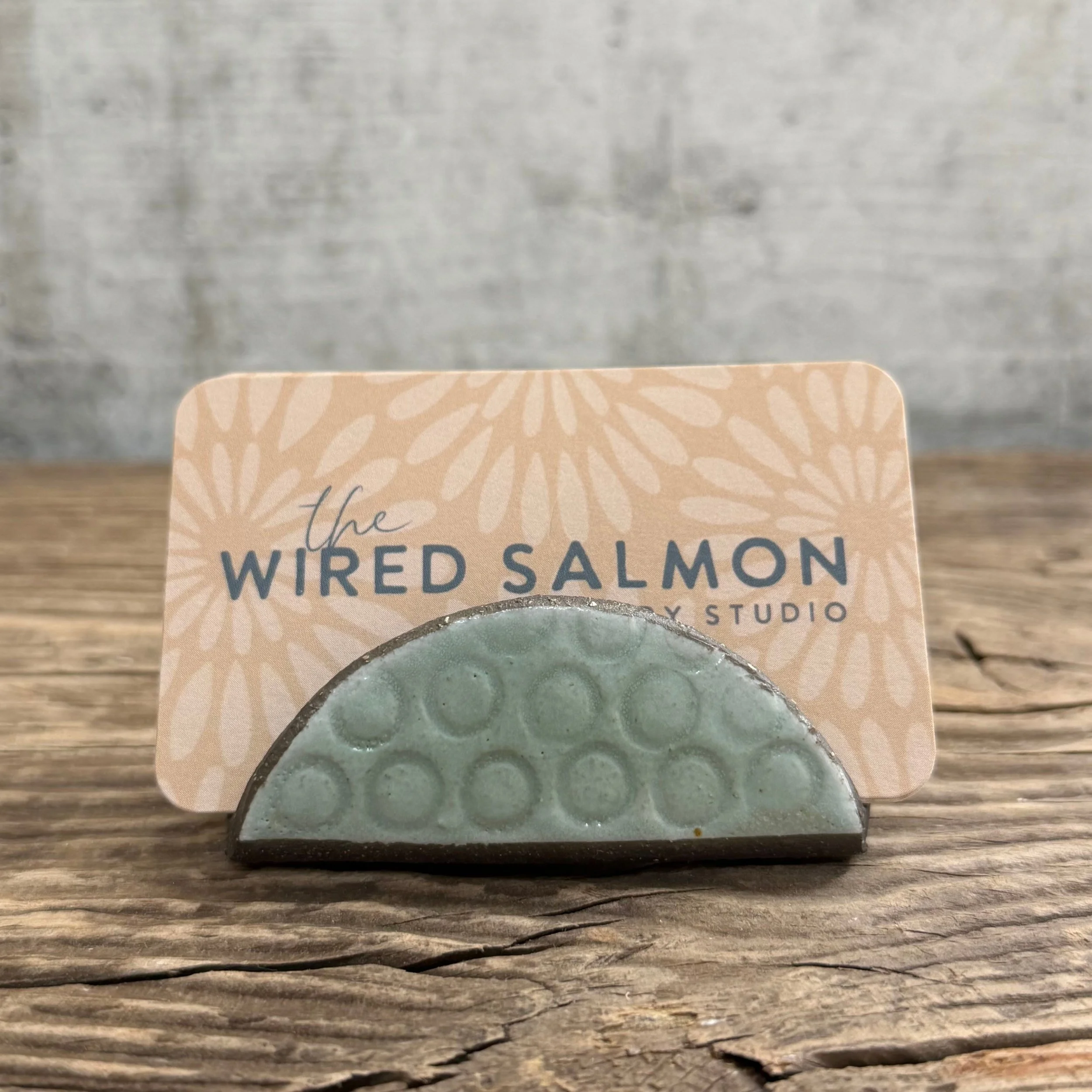 A textured handmade ceramic business card holder made from black clay with a mint finish.