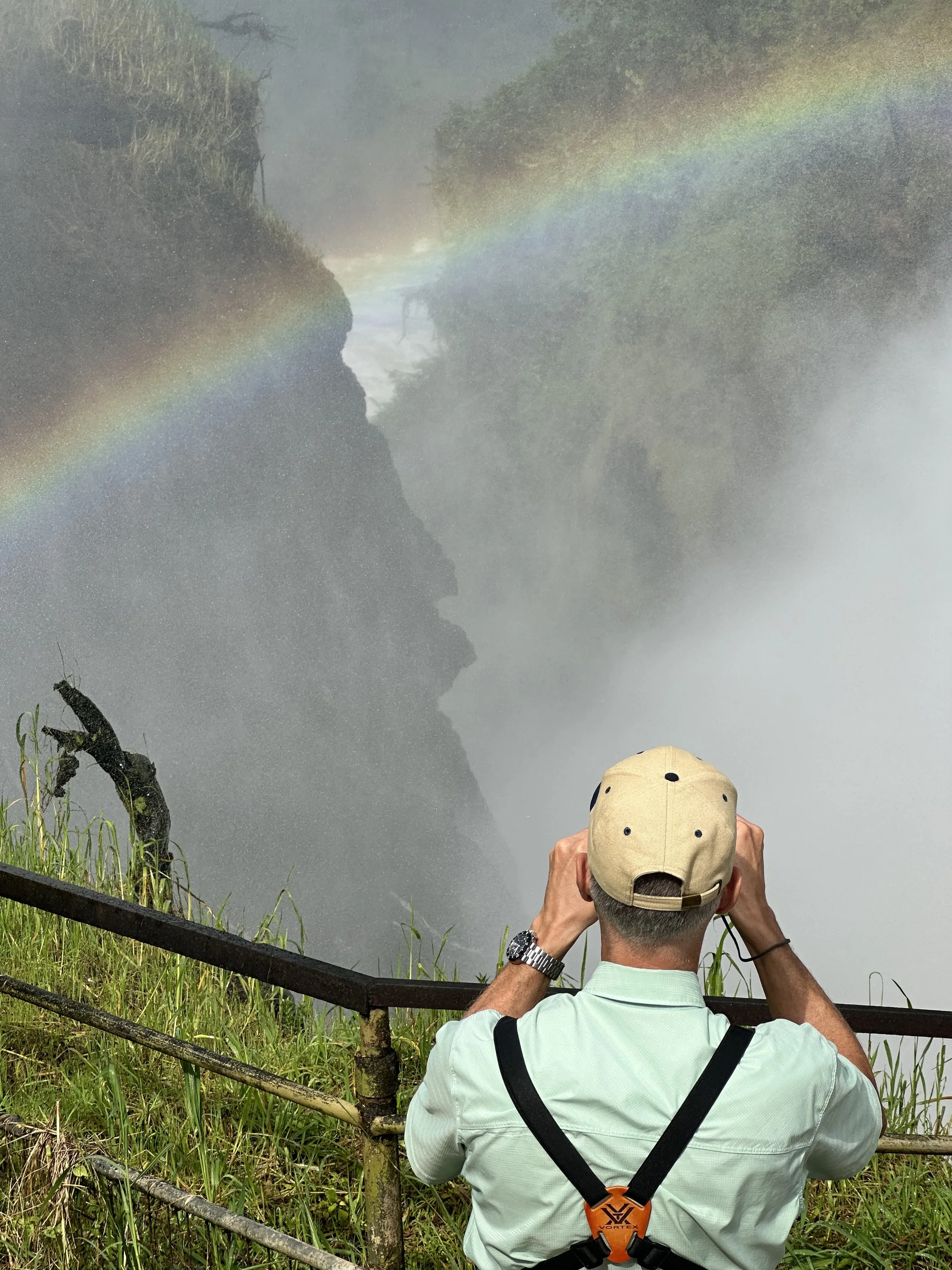 Man photographing incredible waterfall and rainbow on Ugandan safari at the top of Murchison Waterfall