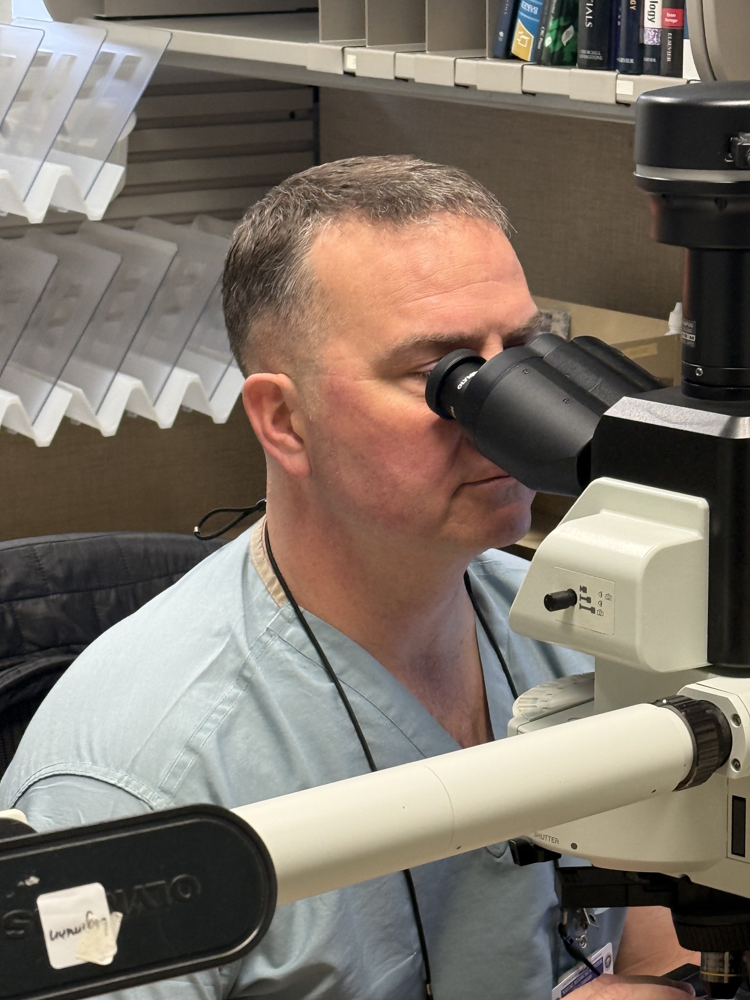 A man in medical scrubs using a microscope in a medical office setting.