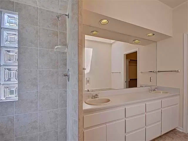 Modern bathroom with a double-sink vanity, mirrored wall, tiled shower area, and built-in lighting.