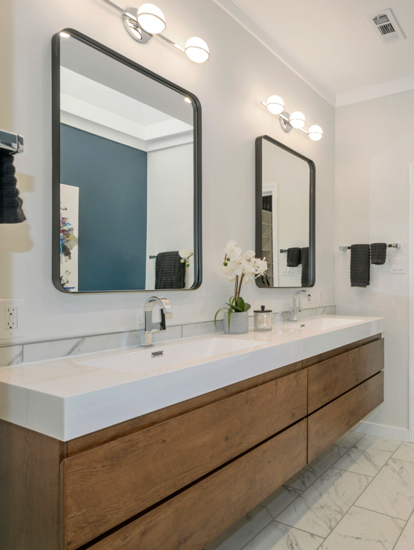 Modern bathroom with dual sinks, large mirrors, and wooden cabinetry. Features marble flooring, sleek faucets, and contemporary lighting. Decorative plant and accessories on the counter.