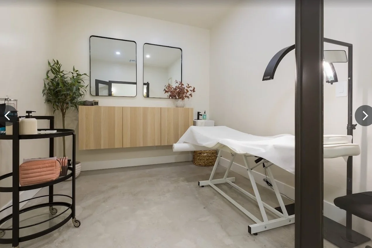 Medical treatment room with examination bed, mirrors, plant, and storage.