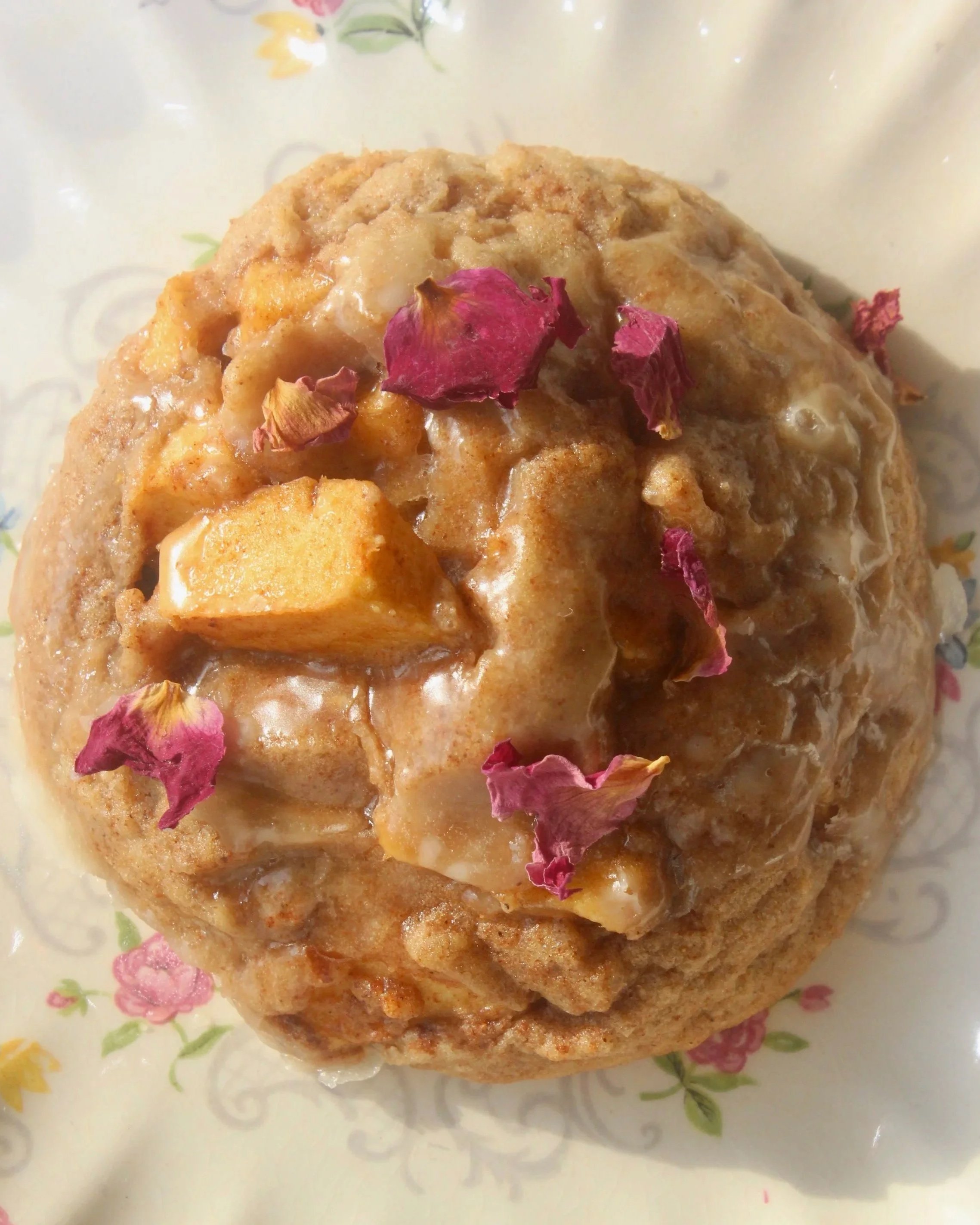 A dessert topped with rose petals, pieces of sweet potato, and a drizzle of syrup on a patterned plate.