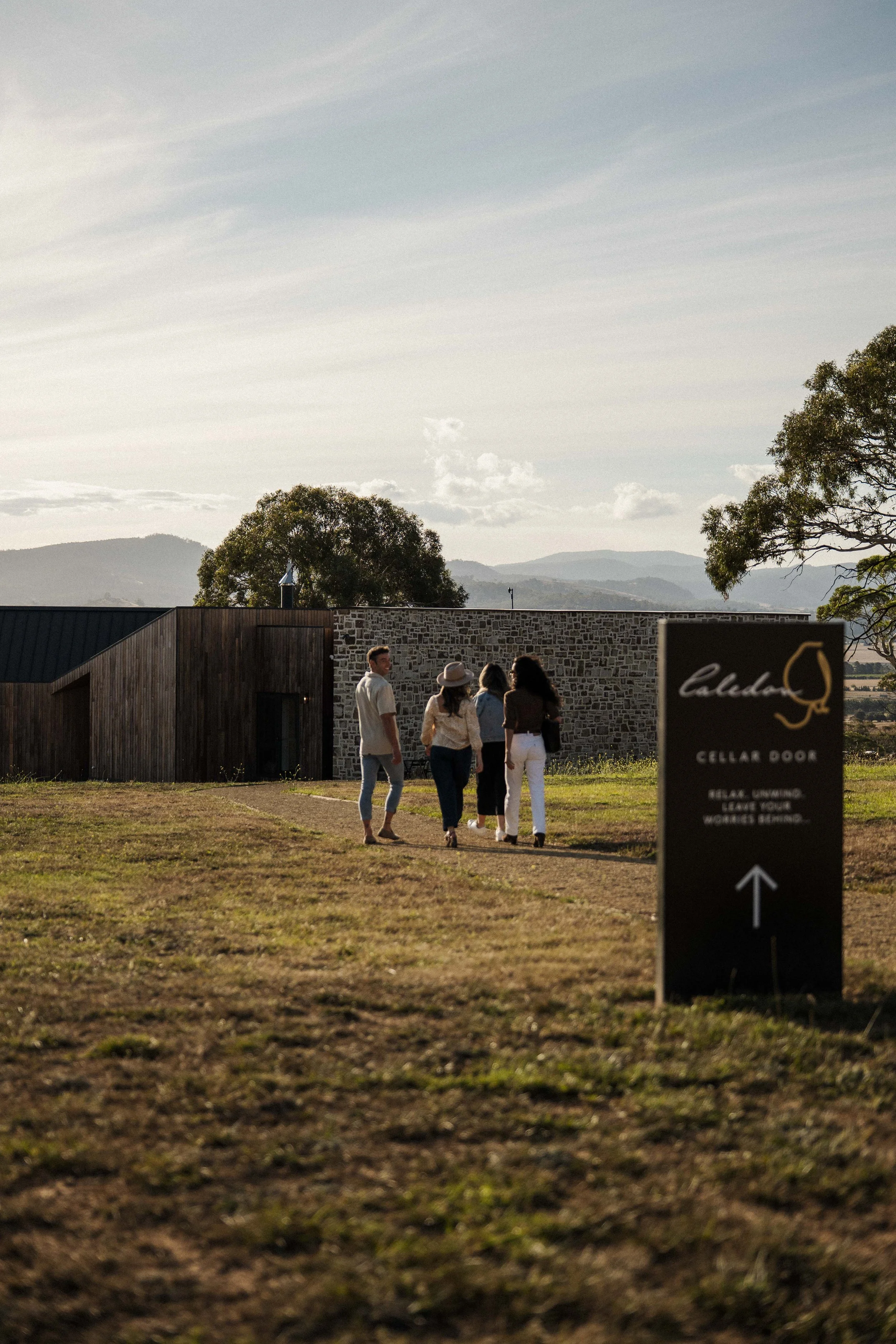 Group of people walking toward a building with a sign that says "Cellar Door" in a rural setting.
