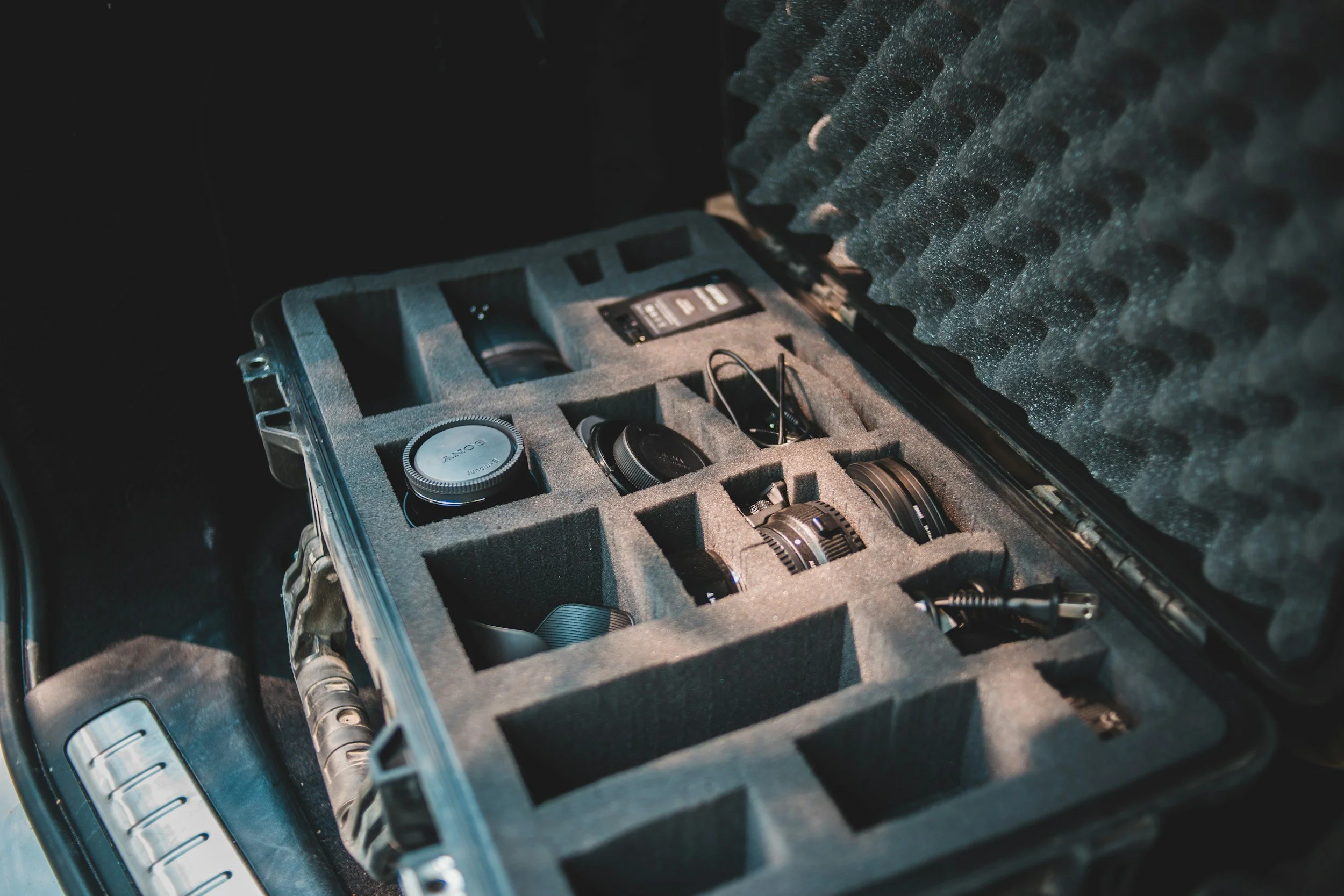 Open hard case containing camera lenses, a camera body, and electronic accessories in foam compartments.