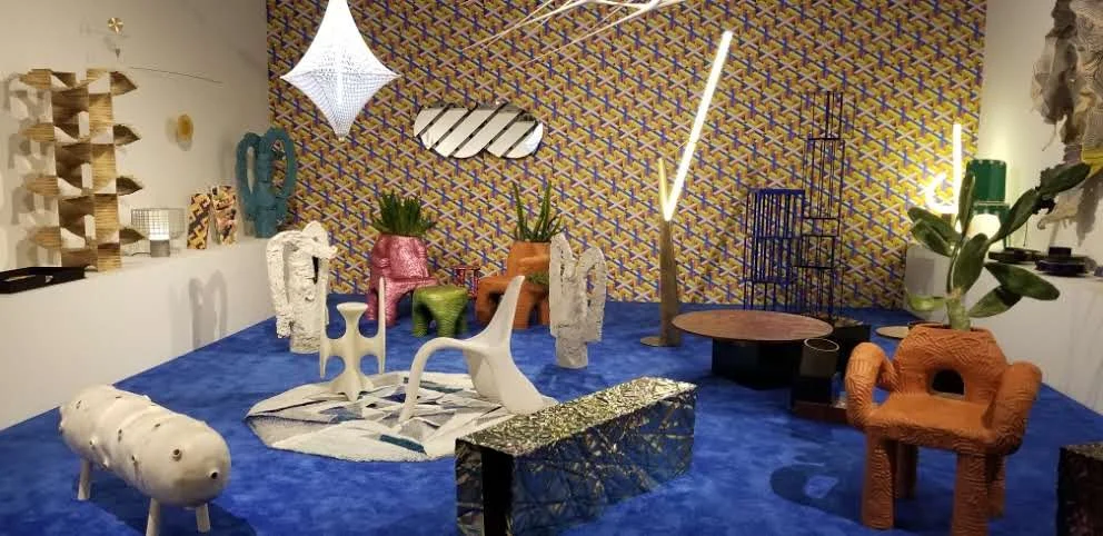 Eclectic art installation featuring colorful sculptures, modern furniture, patterned wallpaper, and decorative lighting.