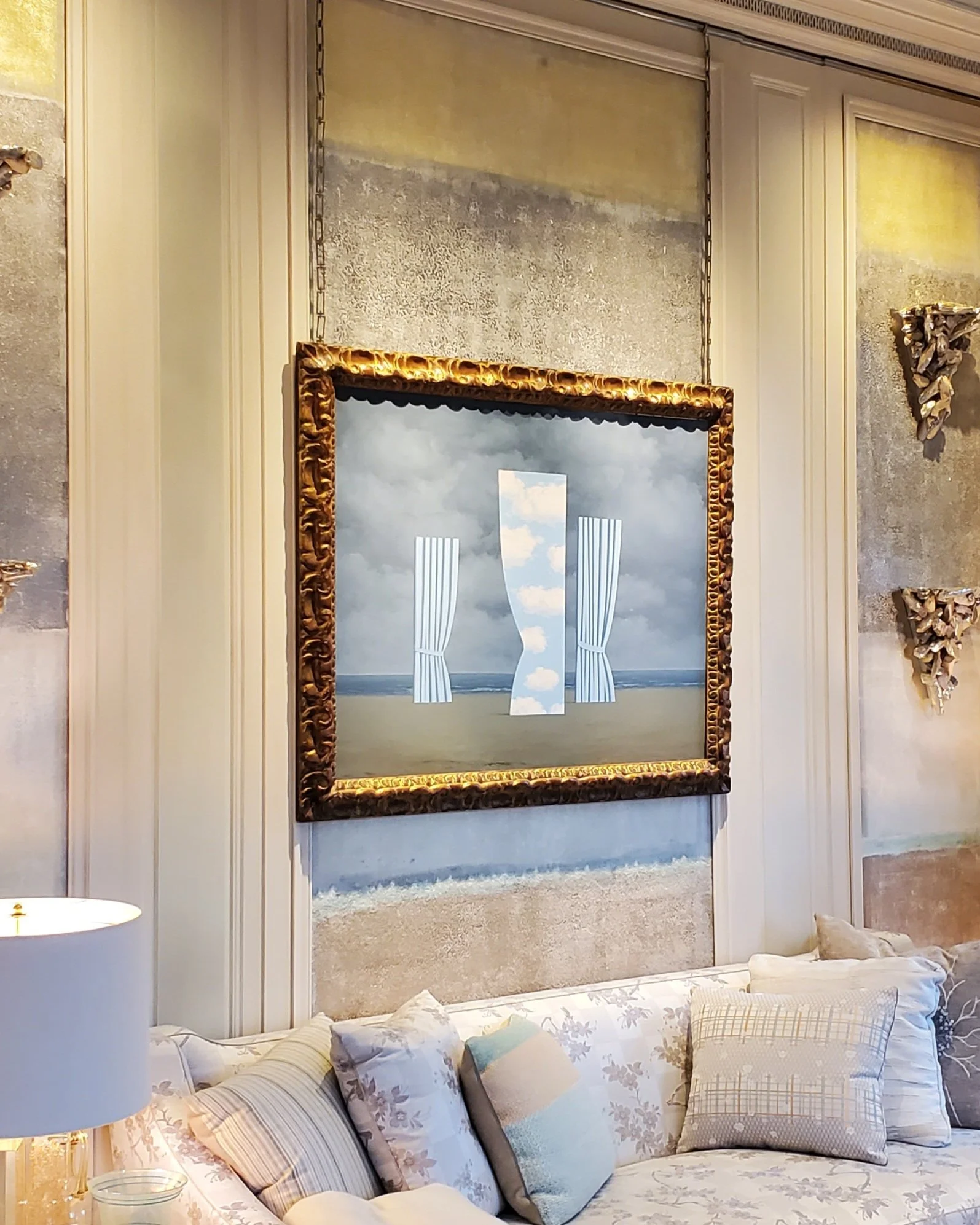 Elegant dining room with a large ornate gold-framed mirror on the wall, a marble fireplace, and a cozy seating area with various pillows.