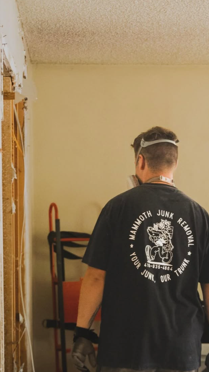 A man with a respirator demolishing a wall with a Mammoth Junk Removal t-shirt on
