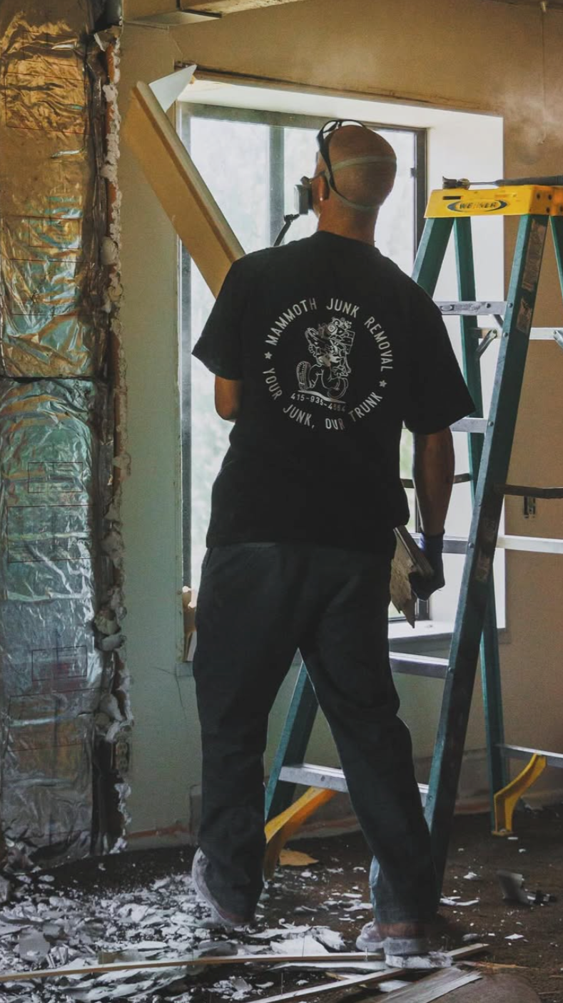 A man with a respirator demolishing a wall with a Mammoth Junk Removal t-shirt on