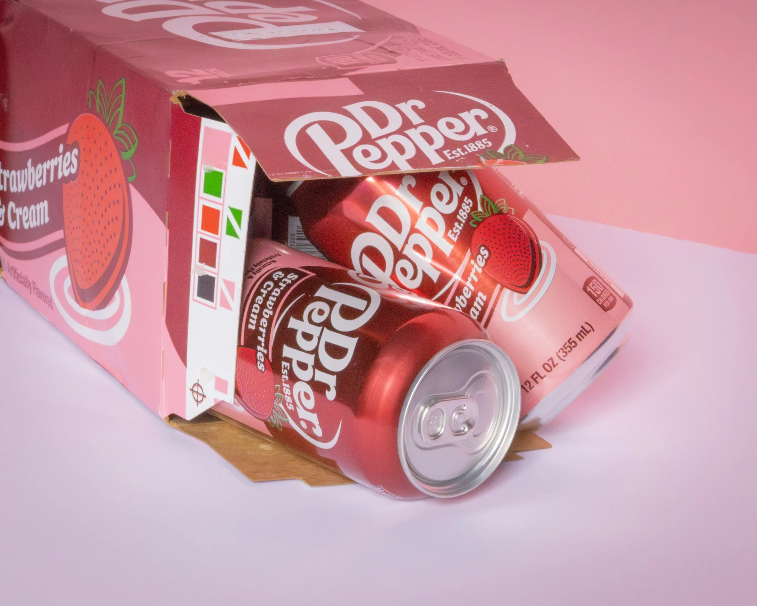 A cardboard box with strawberry-flavored cream containers spilling out, featuring red cans with strawberry images and the Dr Pepper logo on a pink background.