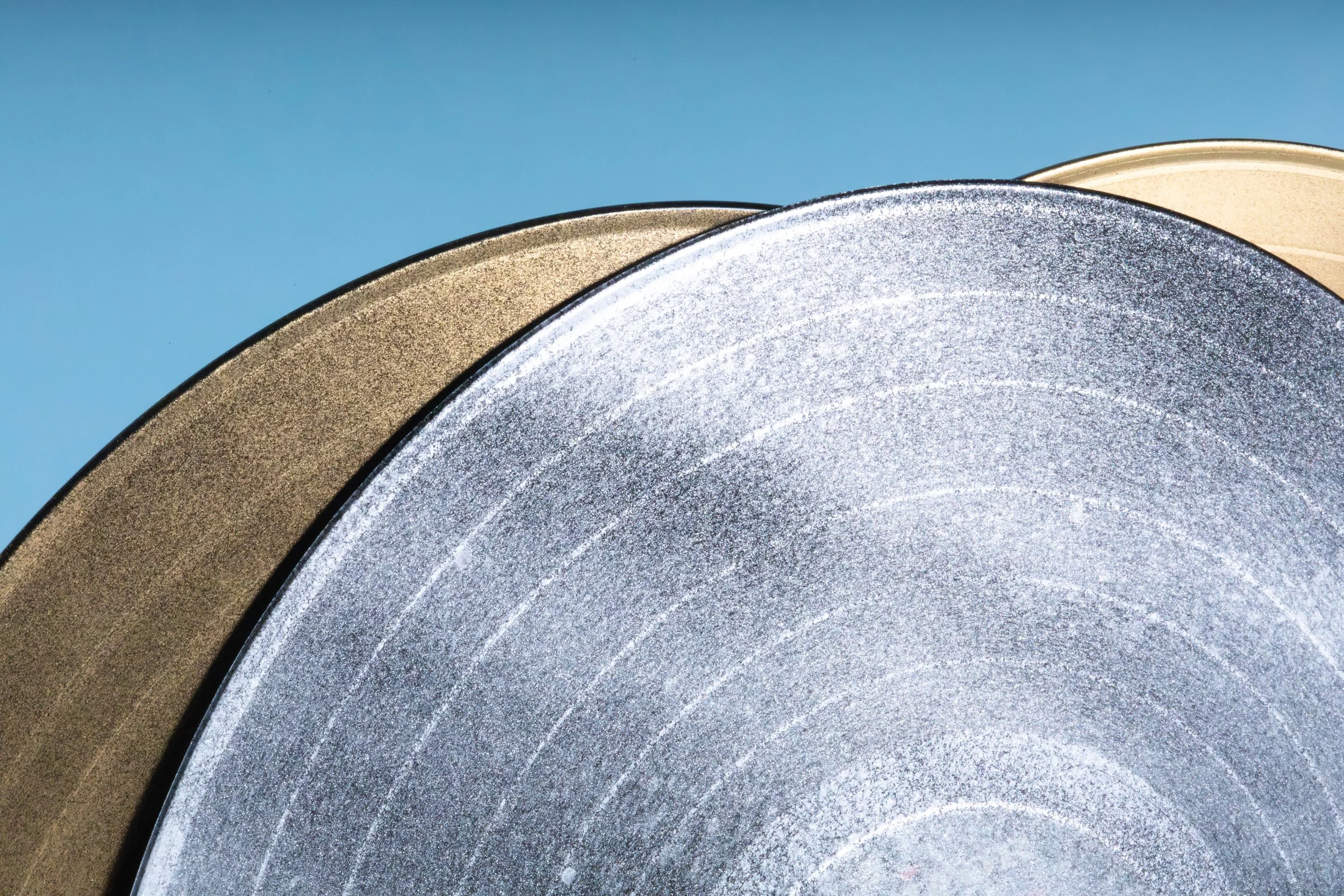 Close-up of the edges of three painted vinyl records stacked together, showing different metallic finishes and textures.