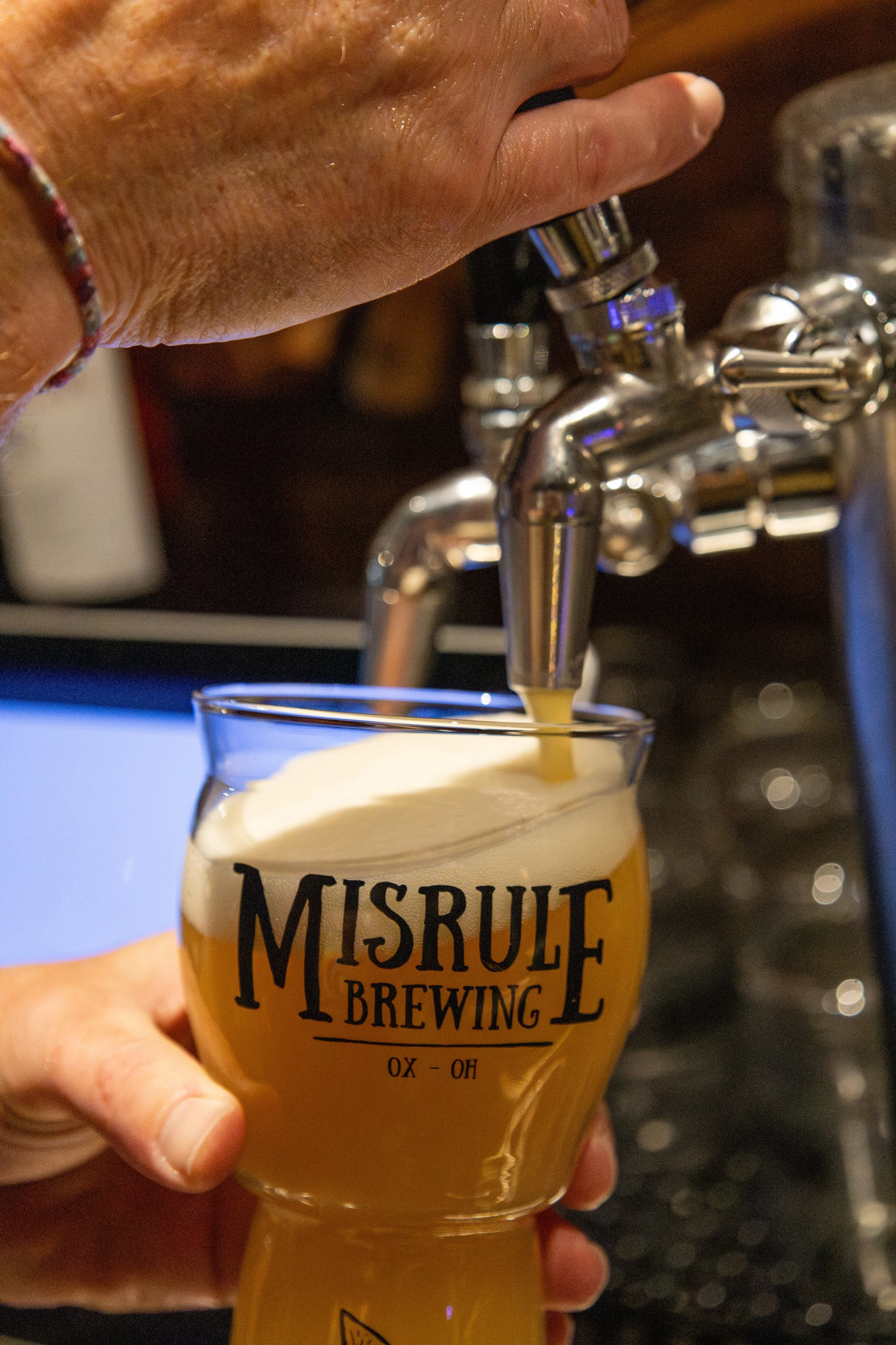 A hand pouring beer from a tap into a glass with "MISRULE BREWING" printed on it.