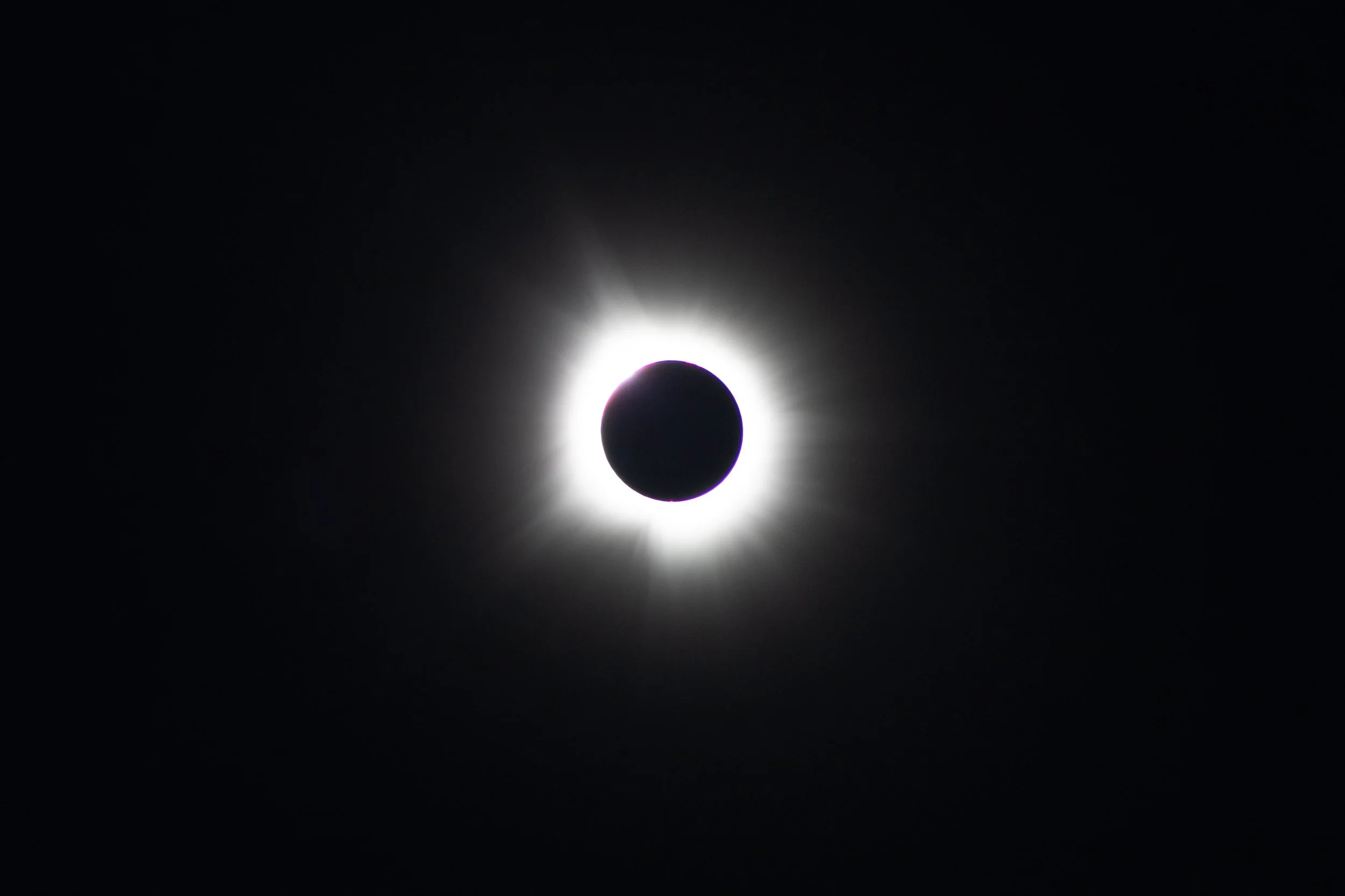 A solar eclipse showing the moon covering the sun, with a bright corona around the dark moon.