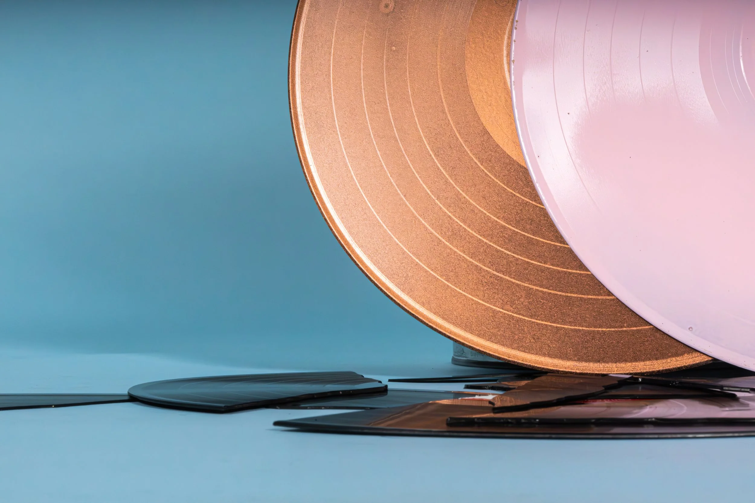 A pink and gold vinyl record is propped up on a light blue surface next to some broken records.