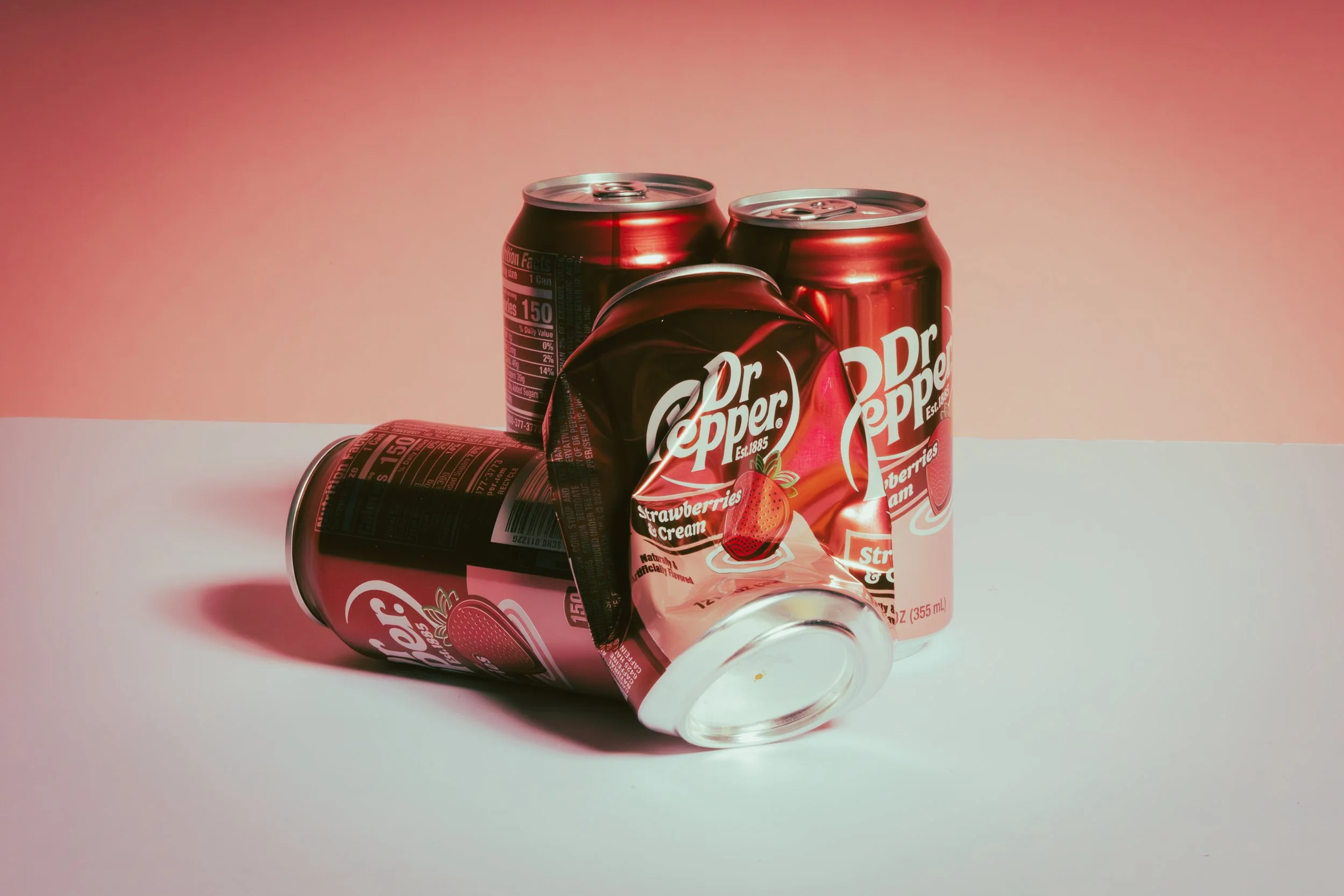 Four cans of Dr. Pepper strawberry and cream soda, with one can lying on its side and partially dented.