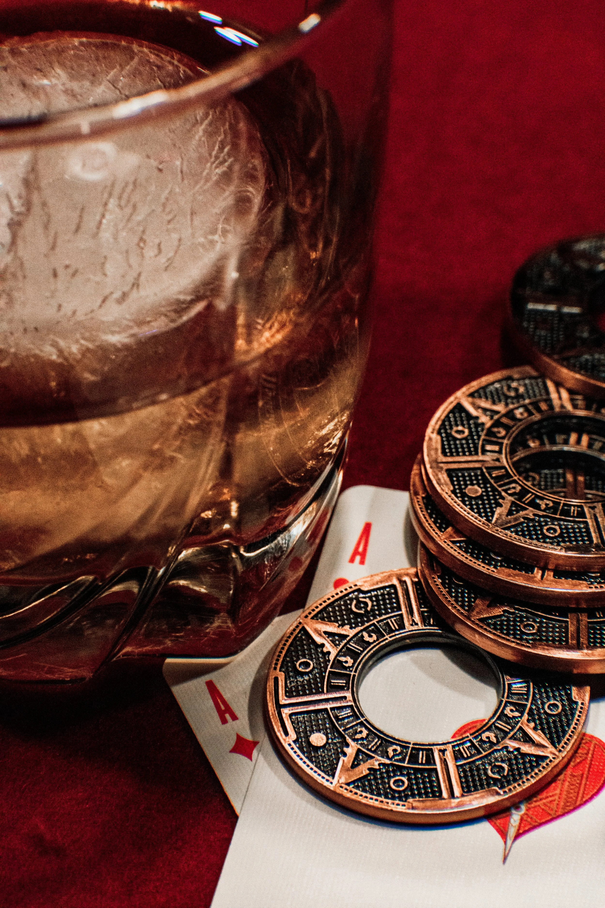 Close-up of a glass of whiskey with ice, poker chips, and playing cards on a red surface.