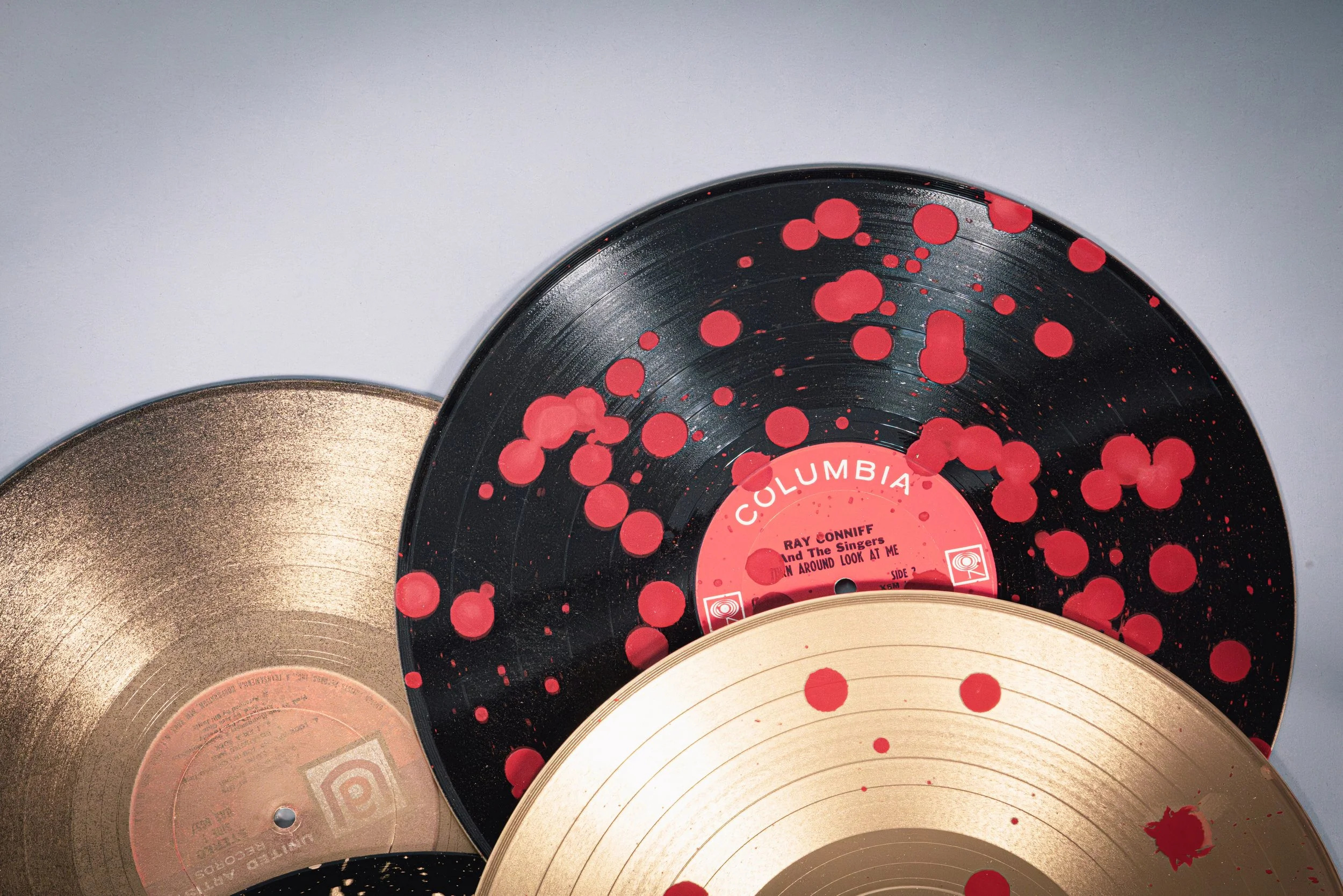 Close-up of three vintage vinyl records, one black with red paint splatters, one gold-colored, and another with a gold spiral pattern, stacked with overlapping edges.