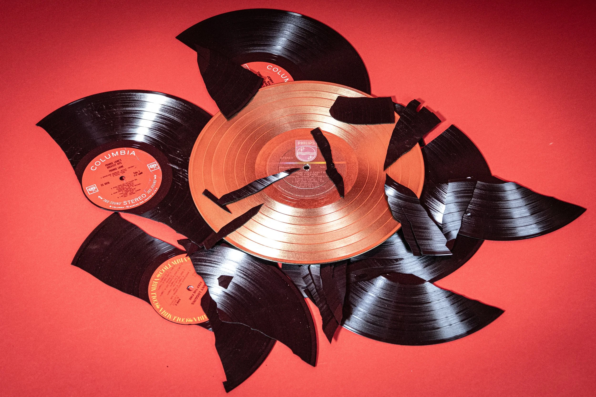 Broken vinyl records on red background, with peeling black and orange labels.
