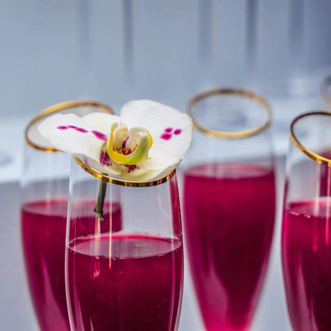 Several tall glasses filled with pink liquid, one with a white orchid flower on top.