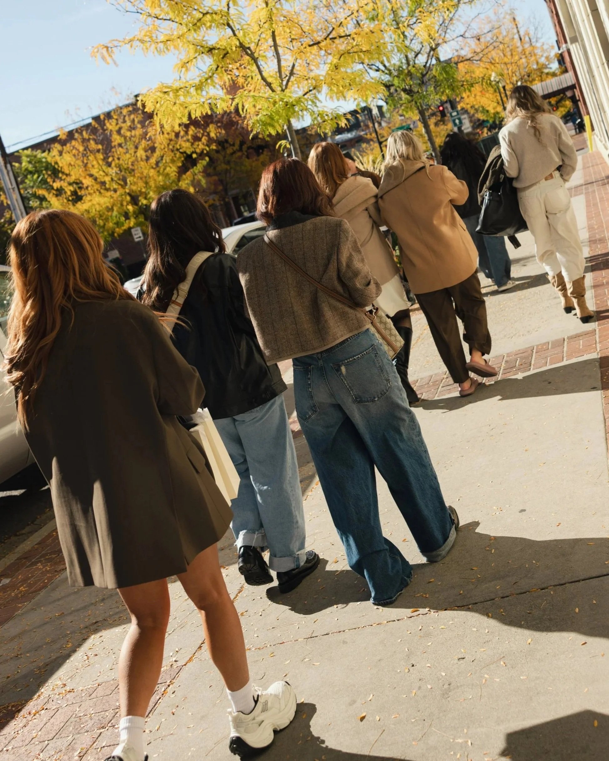 A group of women walking on a sunny sidewalk during autumn with yellow leaves on the trees.