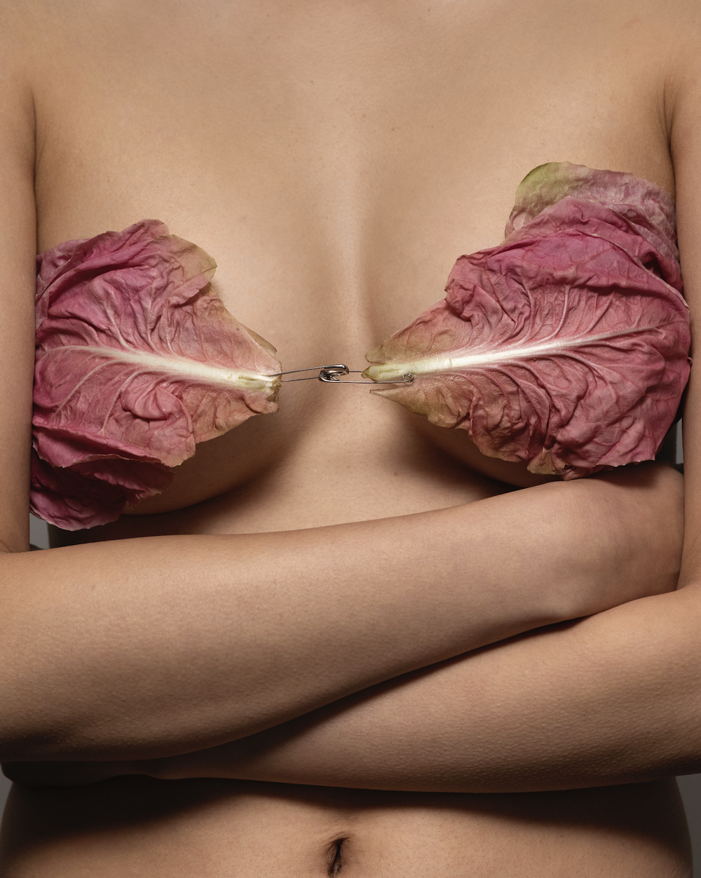 A person holding two large red lettuce leaves with safety pins to their chest, with arms crossed.