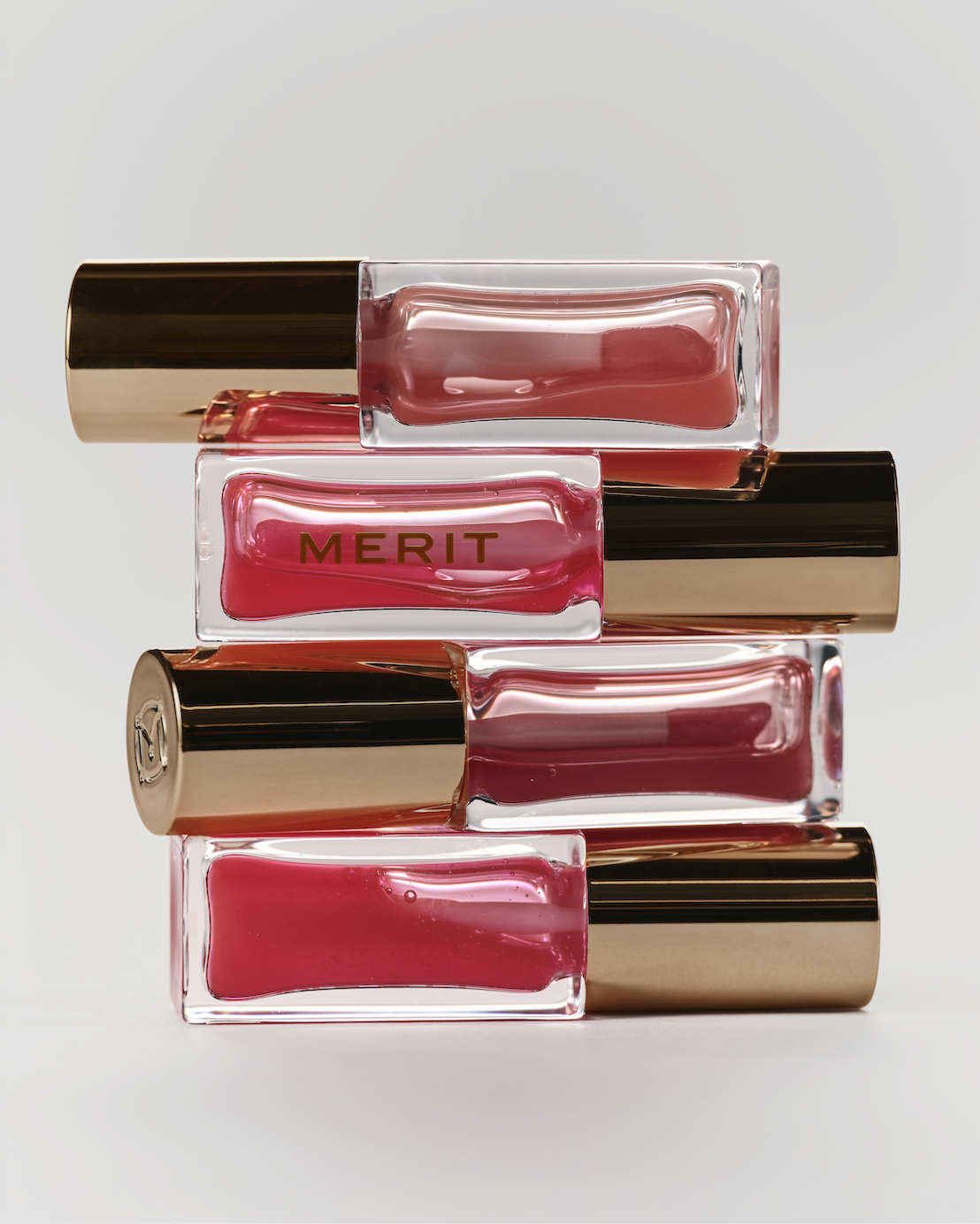 Stacked rectangular glass bottles with pink creamy substance and black-gold caps, one bottle labeled 'MERIT' in gold letters.
