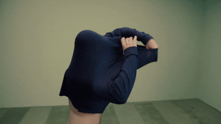 A person holding a large black backpack over their head in a room with green walls and a green carpet.