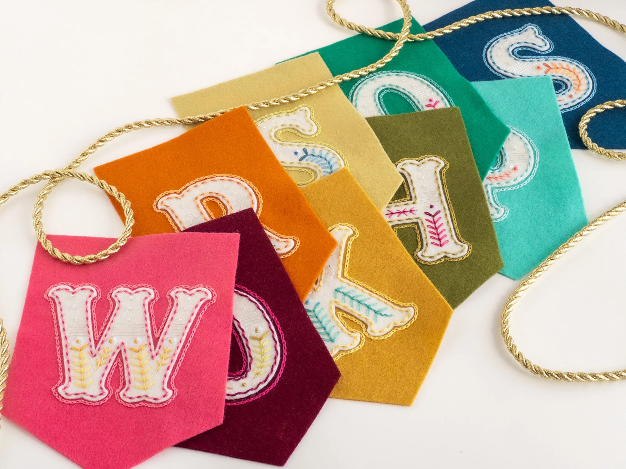 Embroidered felt bunting in rainbow colours spells the word 'workshops'.