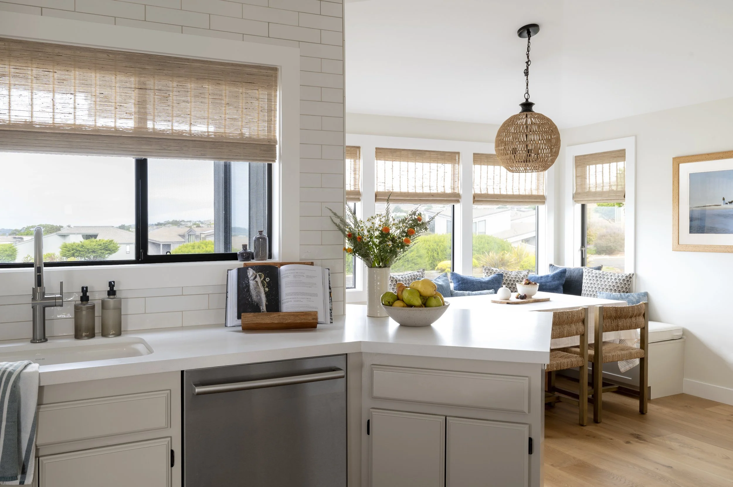 Light-filled Bodega Bay kitchen designed by Arntz Interiors featuring a white island, woven bar stools, natural textures, and coastal-inspired styling.