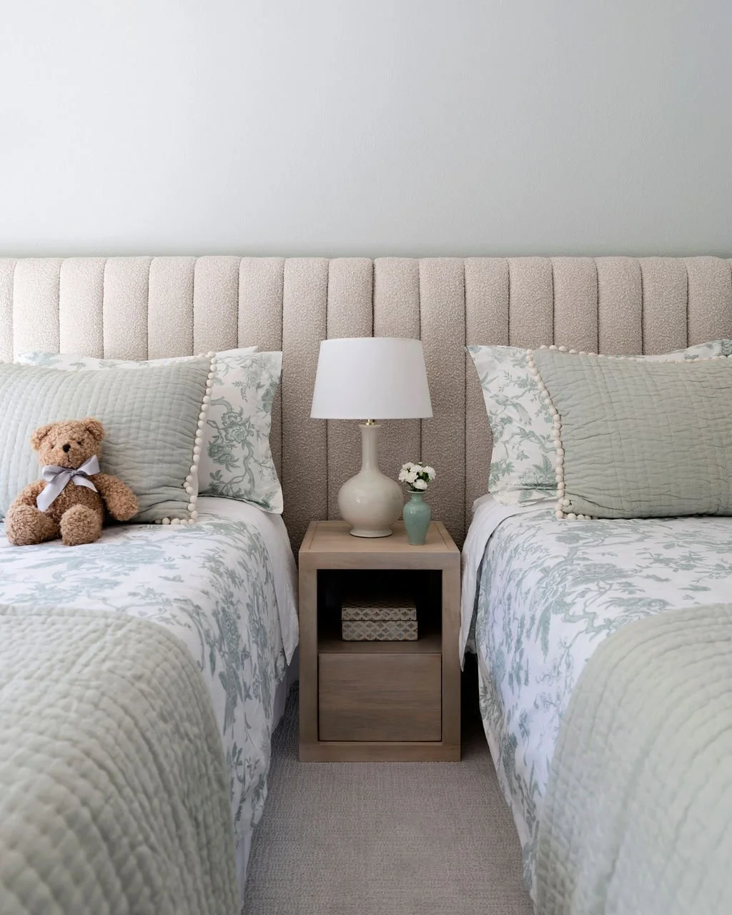 Neutral twin bedroom styled by Arntz Interiors with upholstered headboard, layered botanical bedding, and soft, calming tones.
