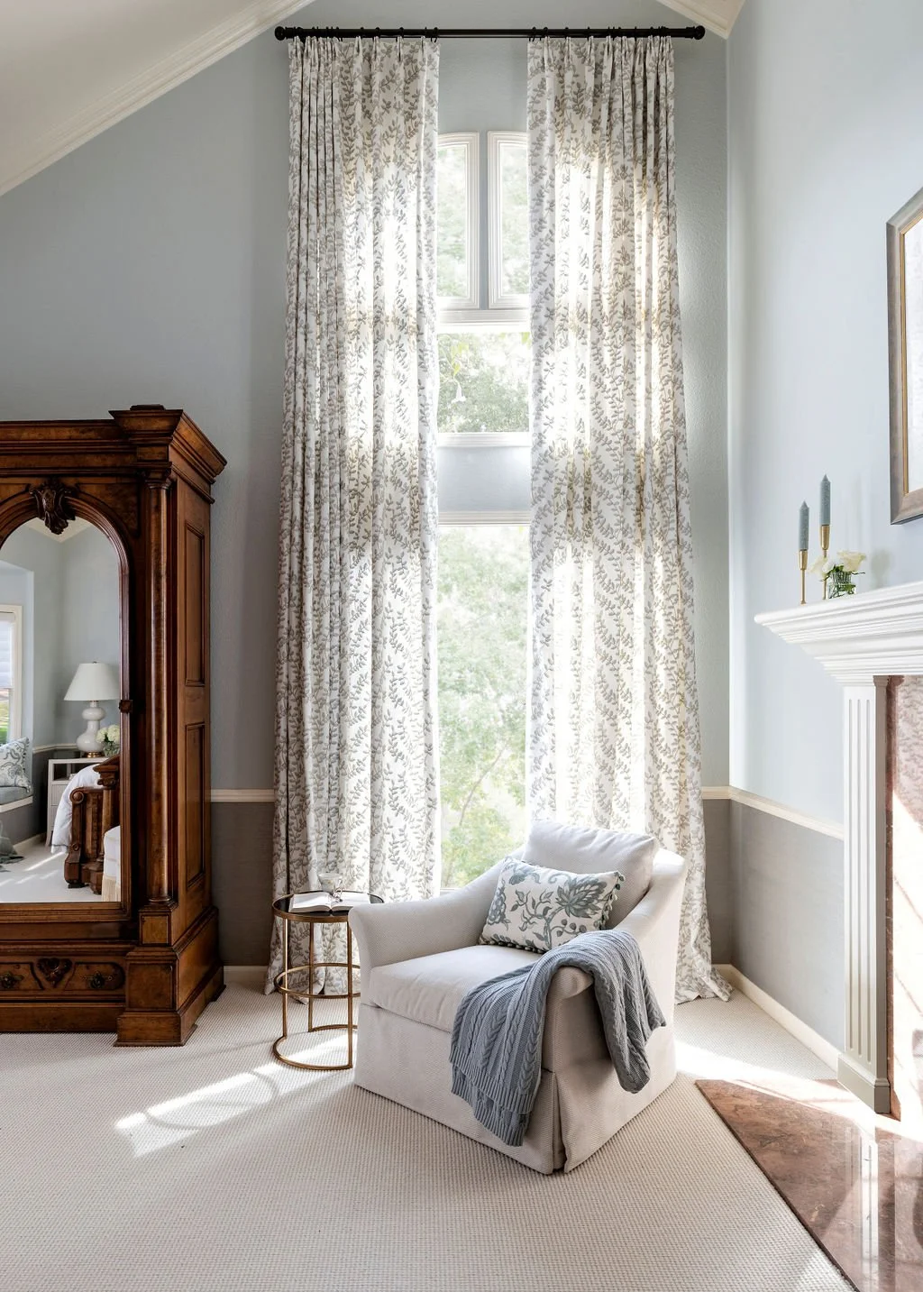 Bay Canyon living space by Arntz Interiors featuring tall patterned drapery, soft blue walls, and a cozy reading chair layered with classic textures.